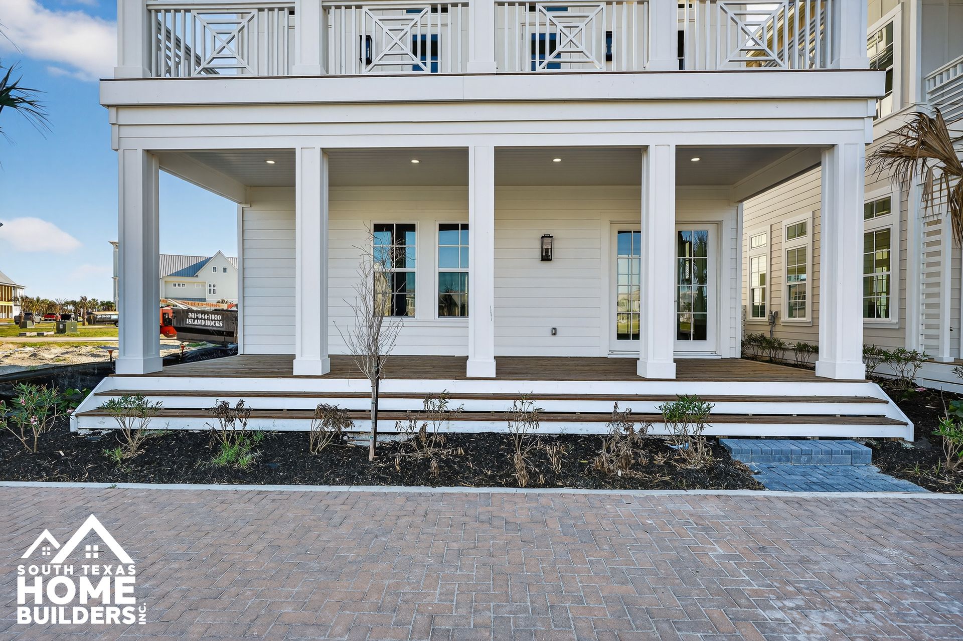 Front view of a white two-story house with porch columns and balcony over a paved driveway