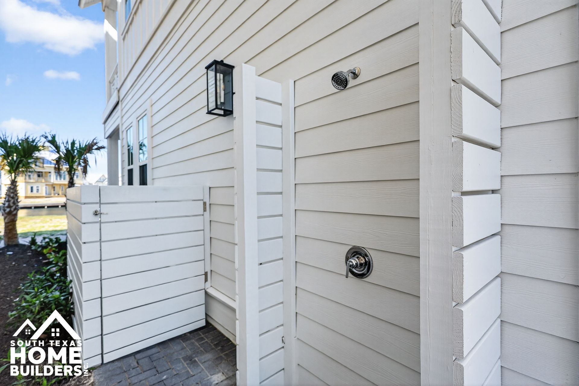 Side view of a white house exterior with a small fenced entry, door, and wall-mounted lights