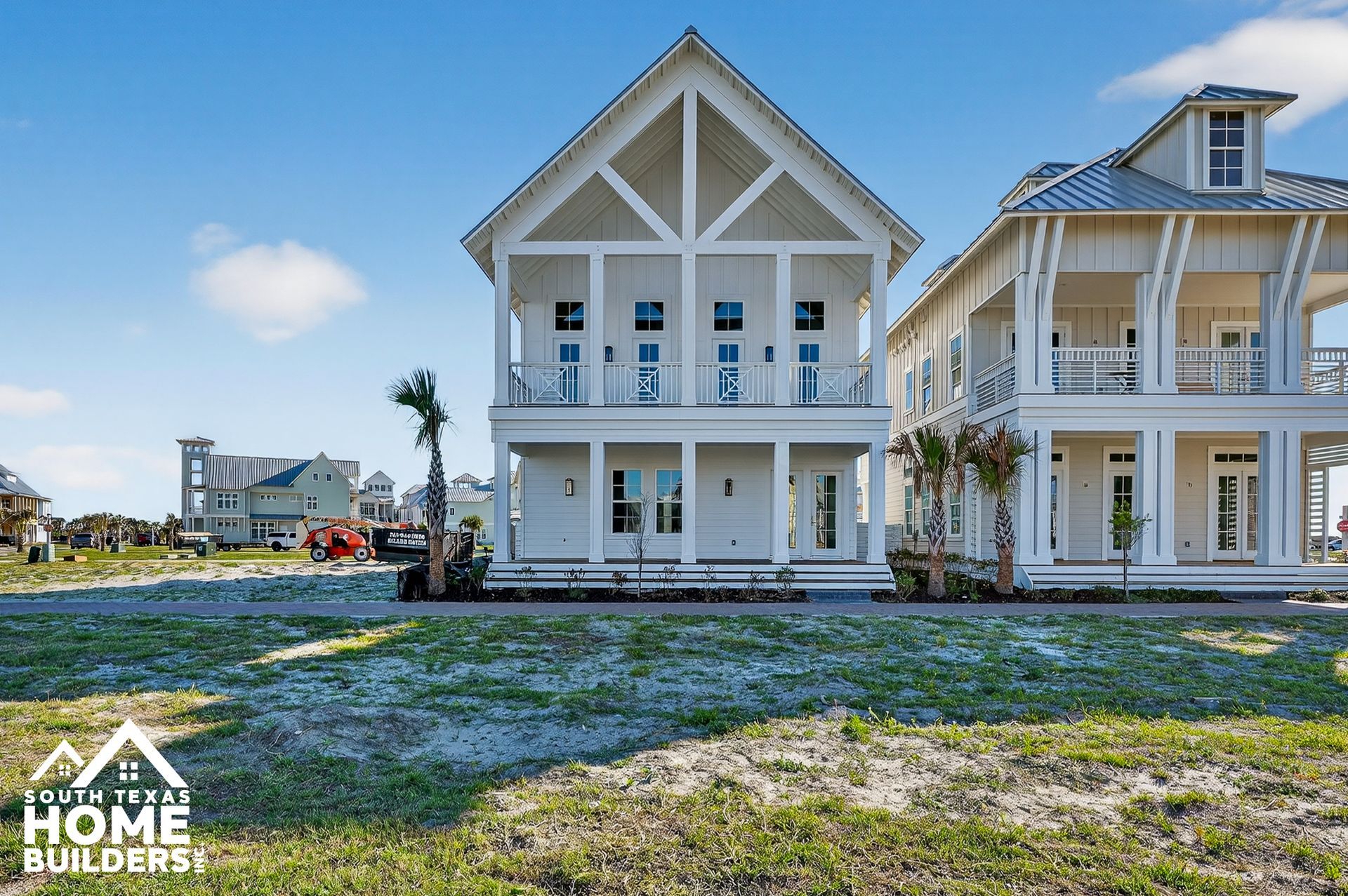 Two-story white beach house under construction beside a similar coastal home on a sunny lot