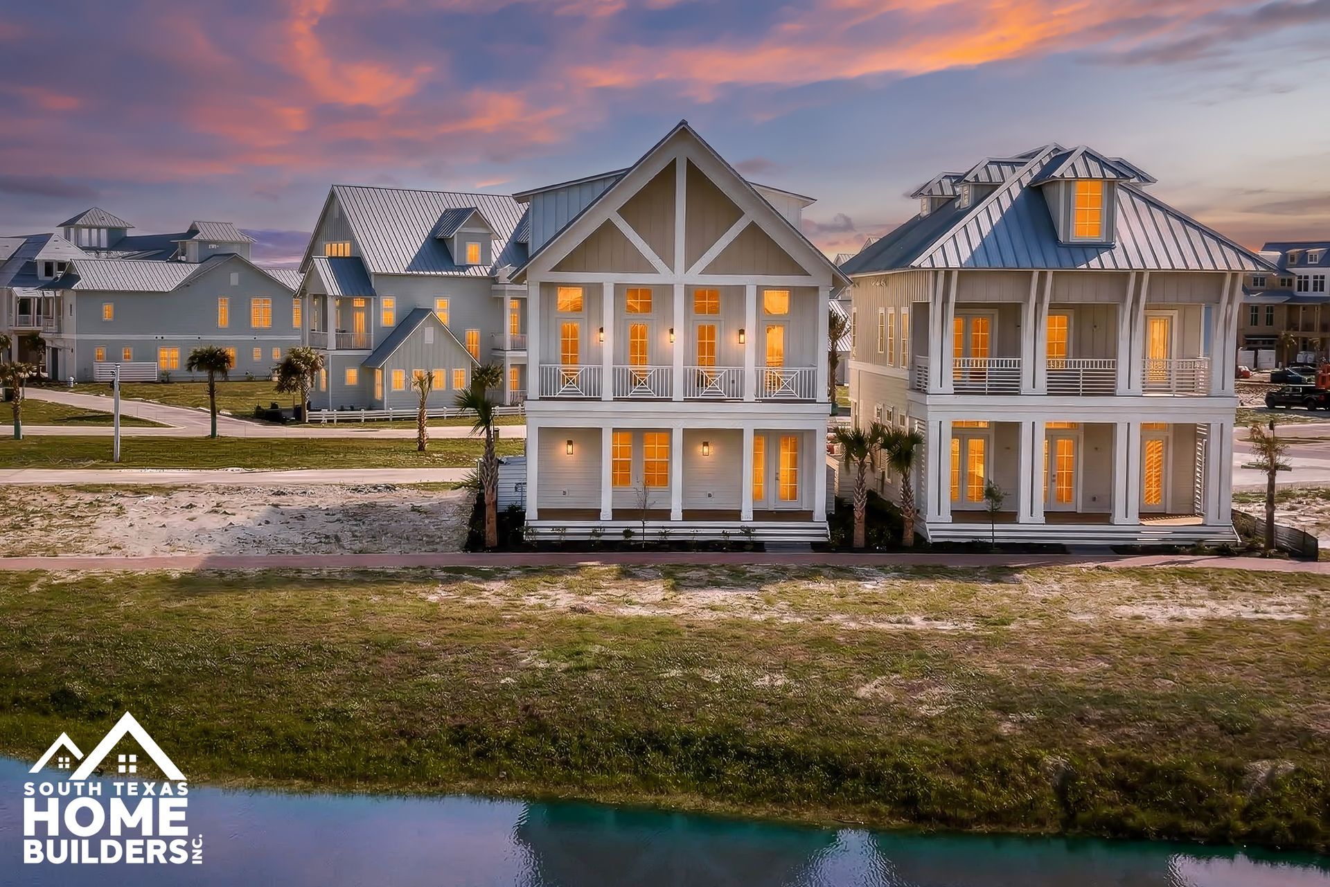Luxury waterfront homes at sunset with lit windows and a Home Builders logo in the corner