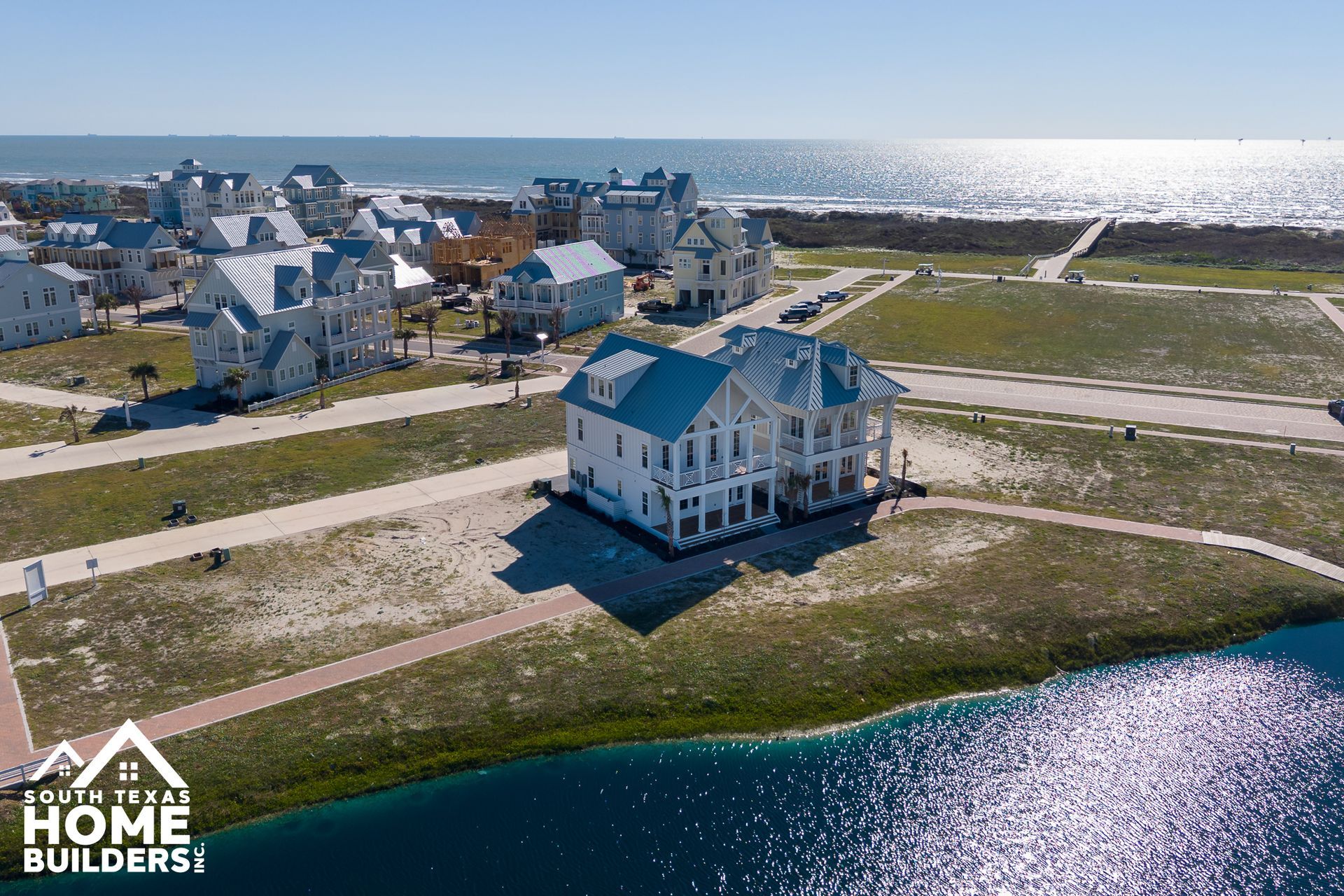 Aerial view of a white beachfront house near water, with several homes and roads along the coast.