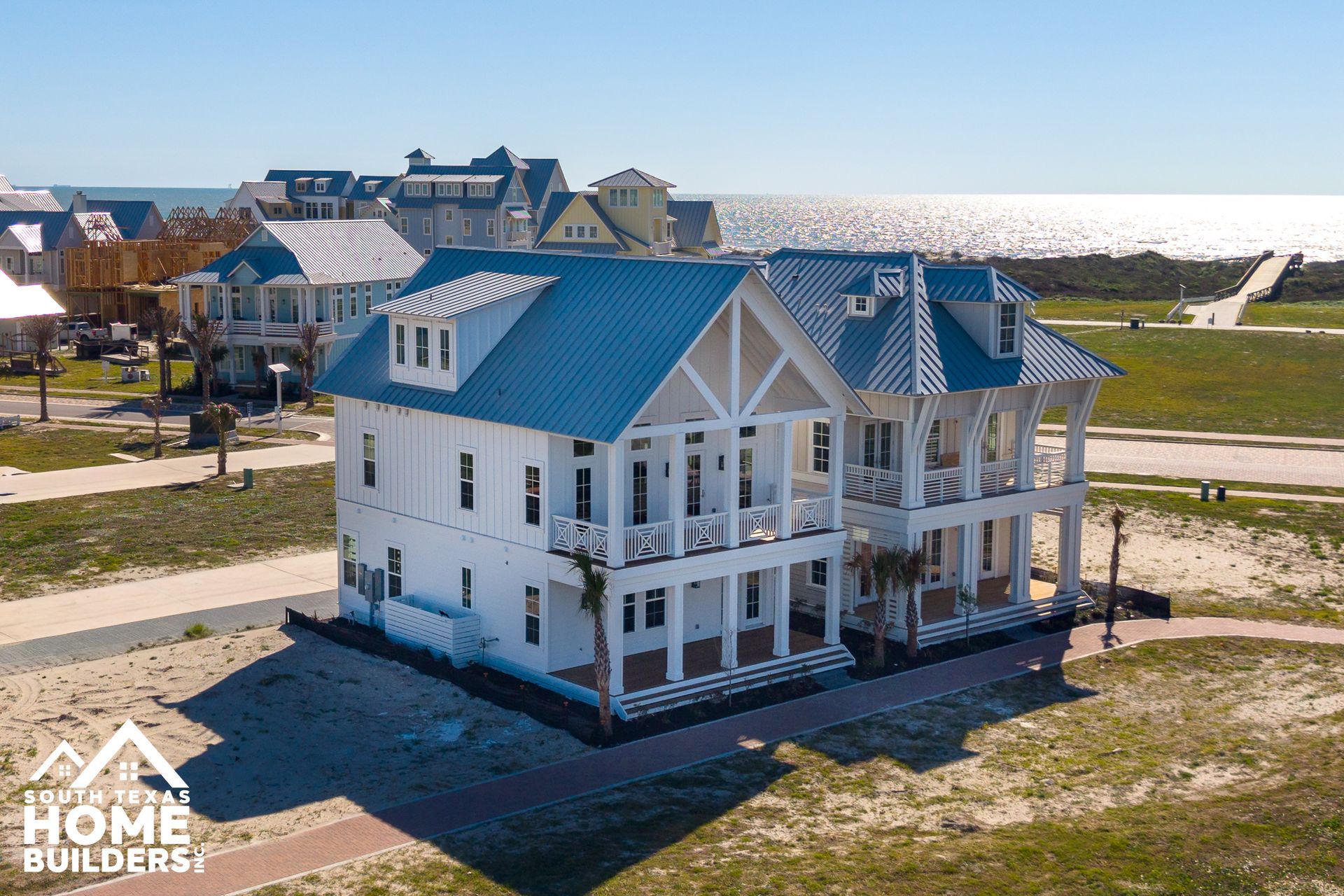 White two-story house with a blue roof in a new coastal neighborhood under a clear sky