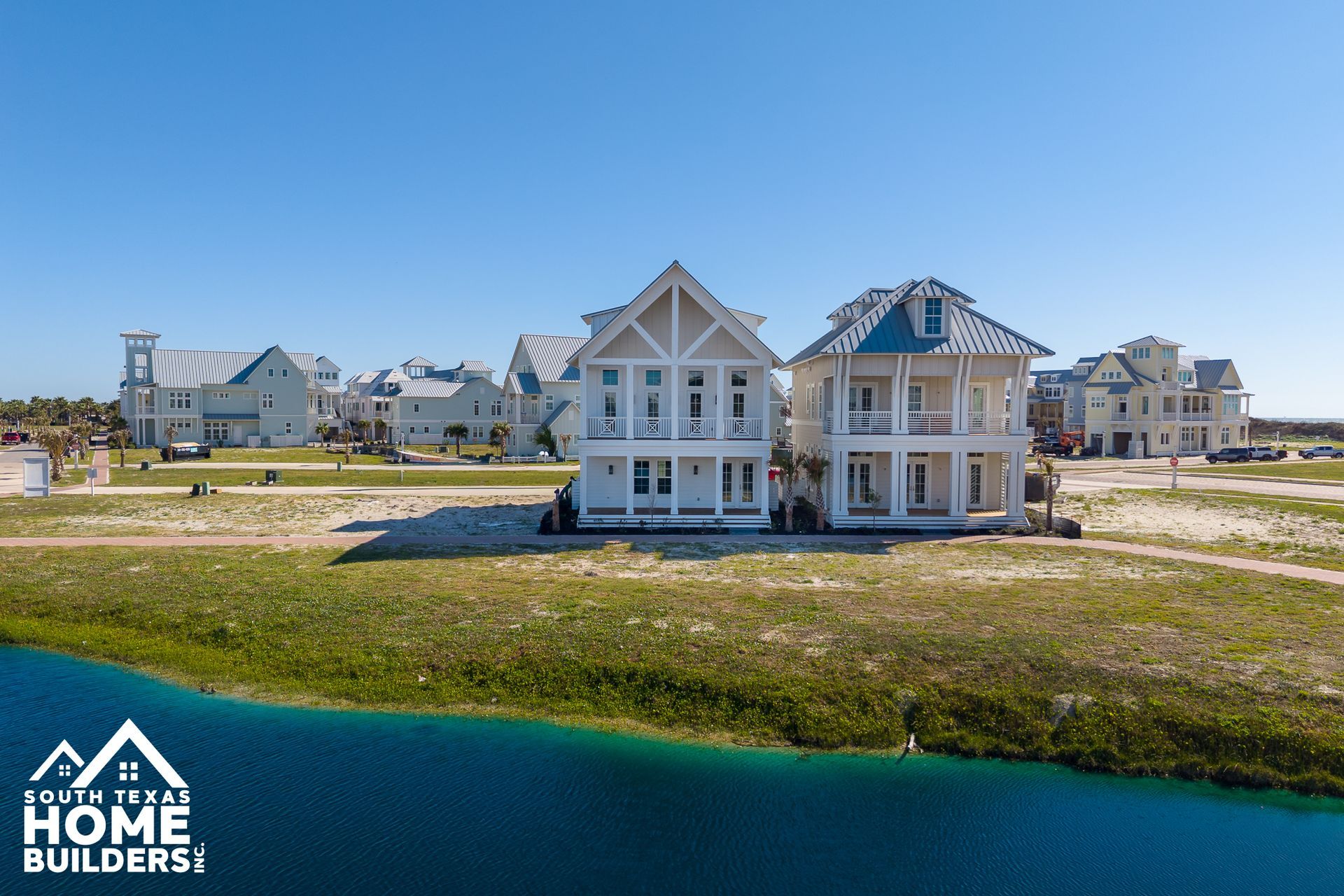 New waterfront homes under construction beside a blue lagoon under clear sky