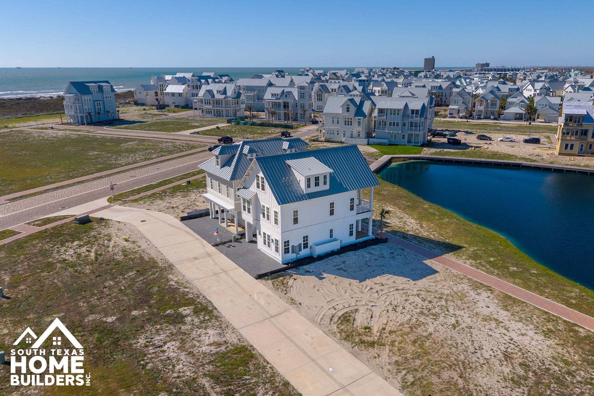 Aerial view of a white house by a pond in a coastal neighborhood under construction