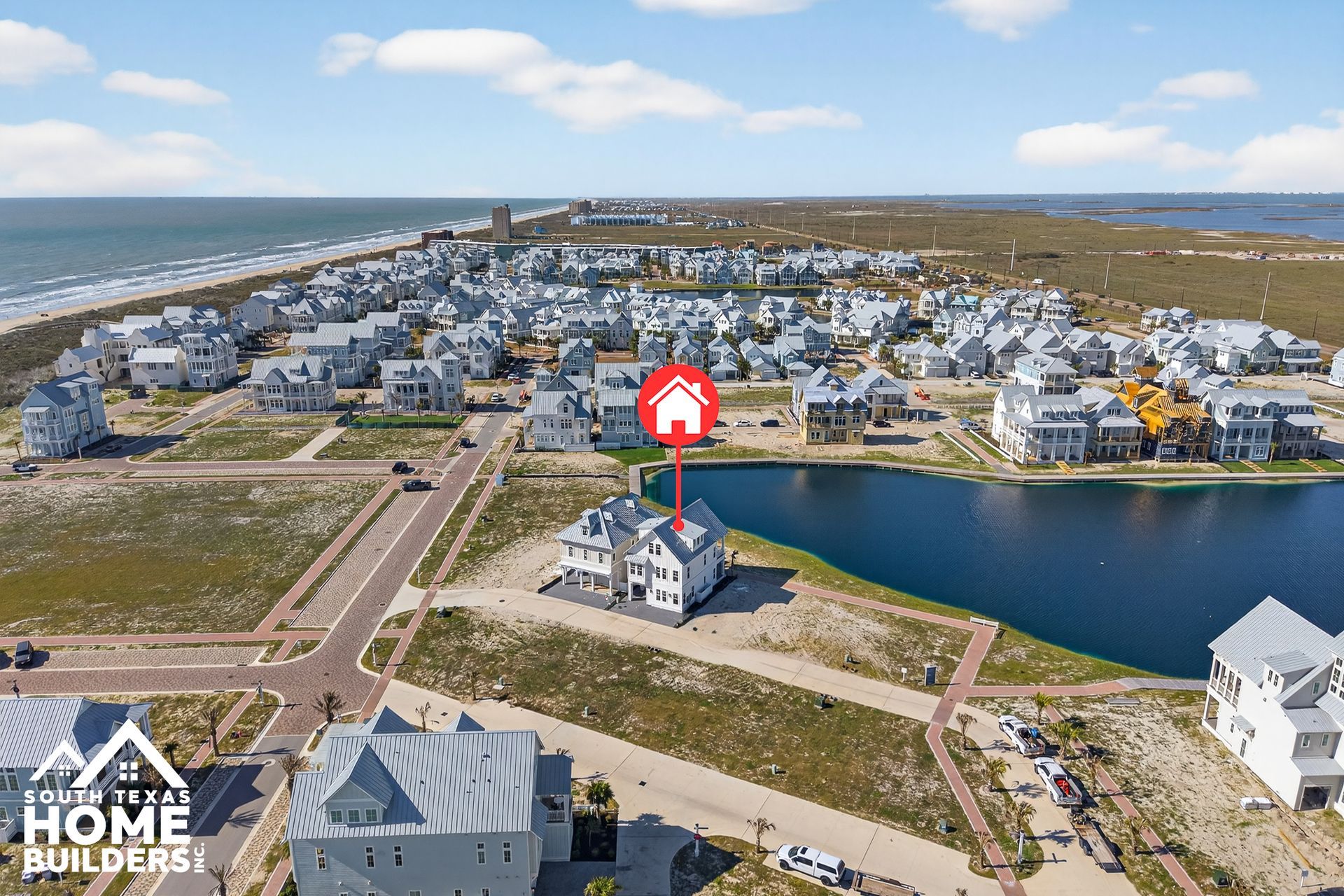 Aerial view of a coastal neighborhood with homes, roads, and a pond near the ocean