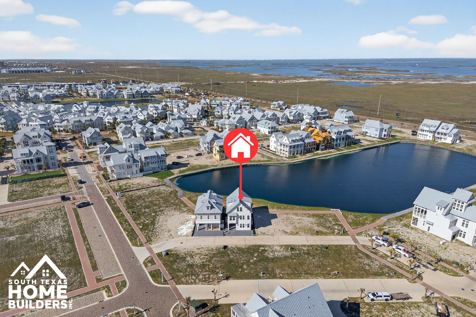 Aerial view of a waterfront neighborhood with houses, roads, and a central home highlighted by a red marker.