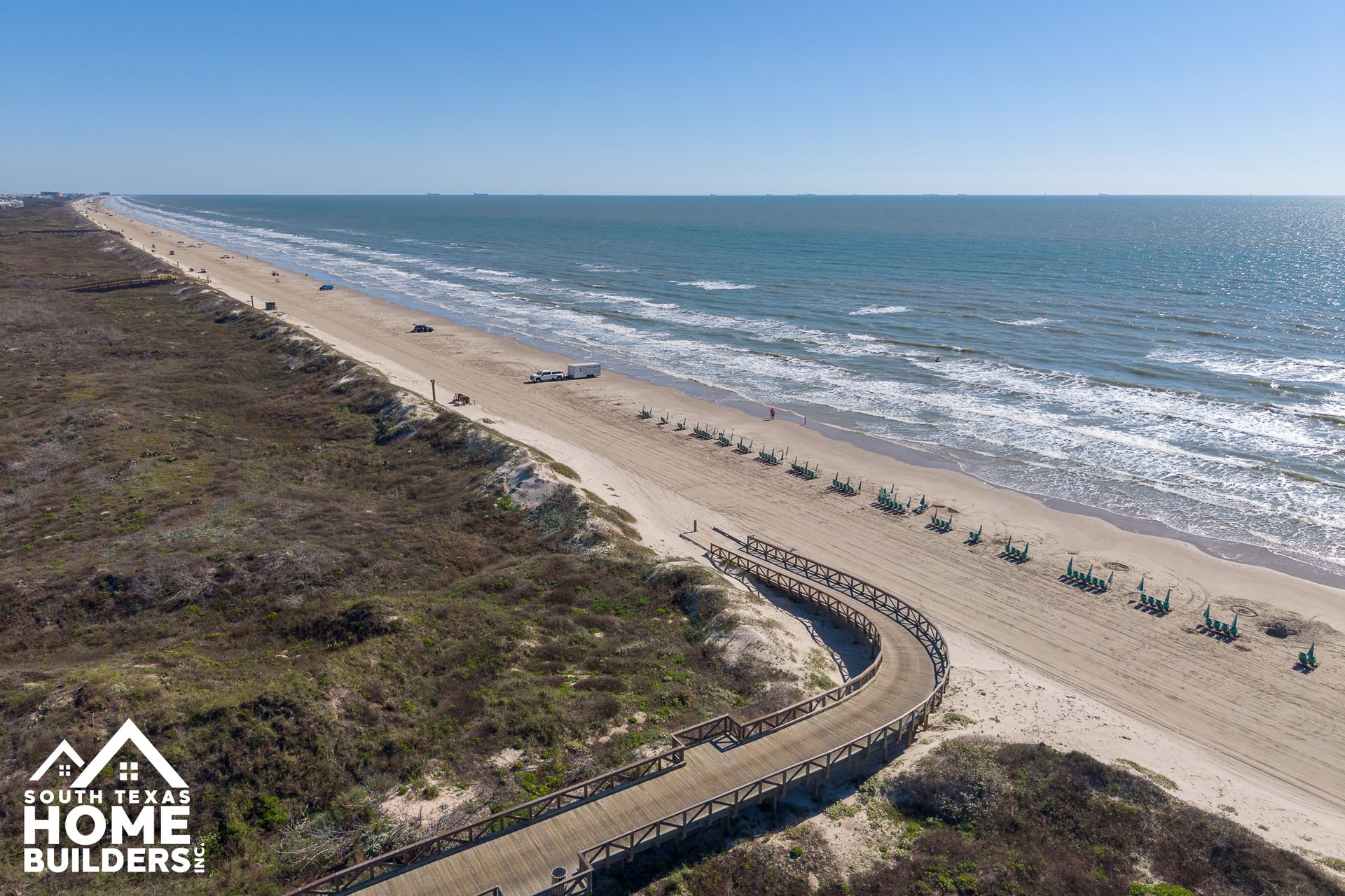 Aerial view of a sandy beach with ocean waves and a winding wooden boardwalk through dunes