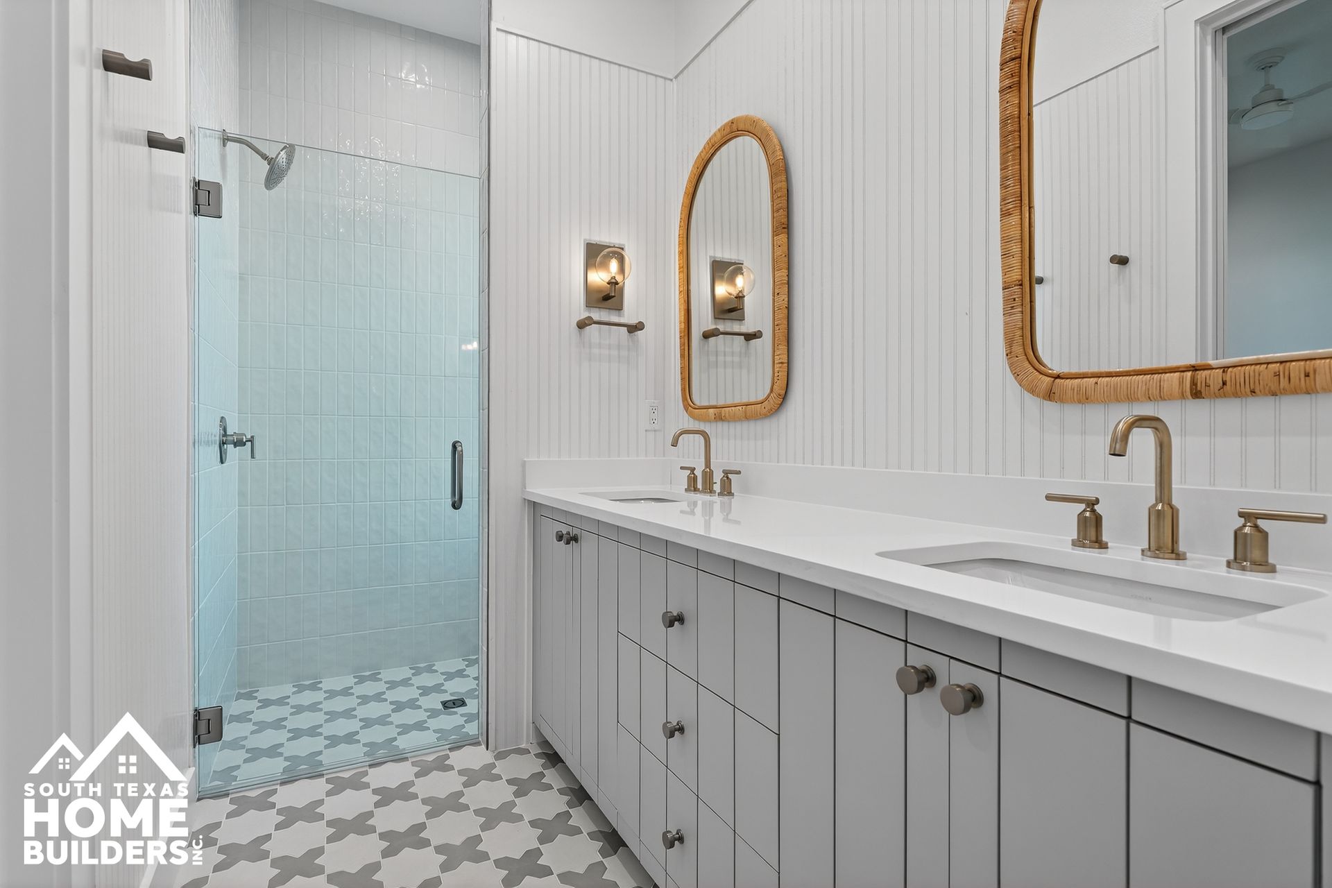 Bright white bathroom with double vanity, gold mirrors, and glass shower with blue tile floor