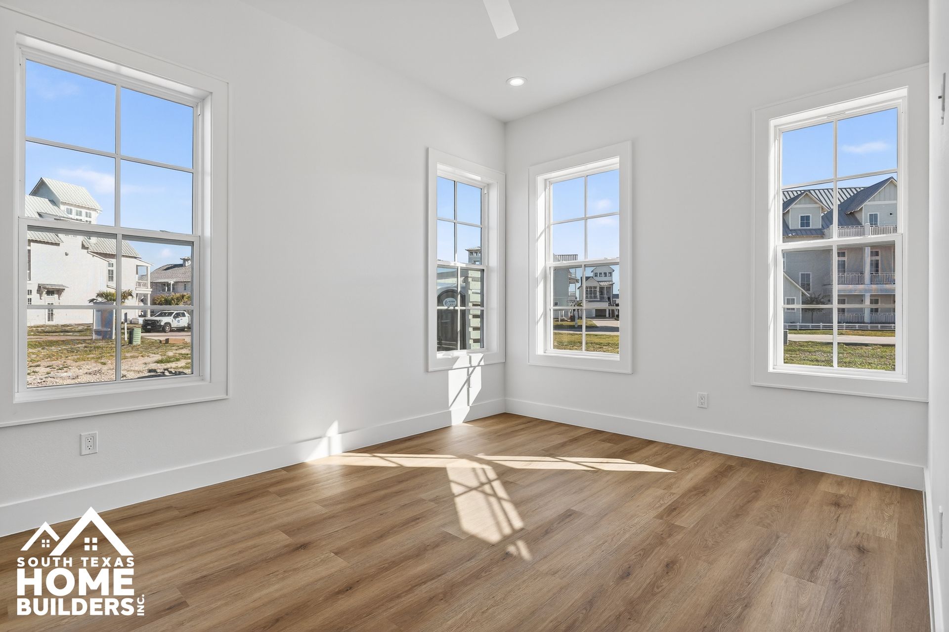 Bright empty room with white walls, large windows, and wood floors with sunlight streaming in.