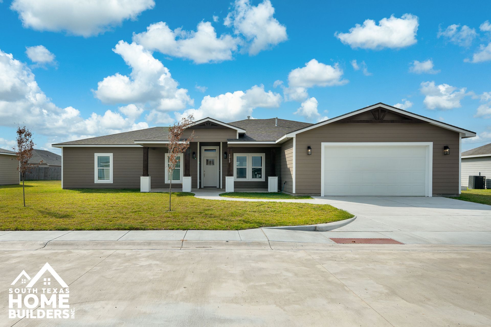 Brown house with white garage door and blue sky.