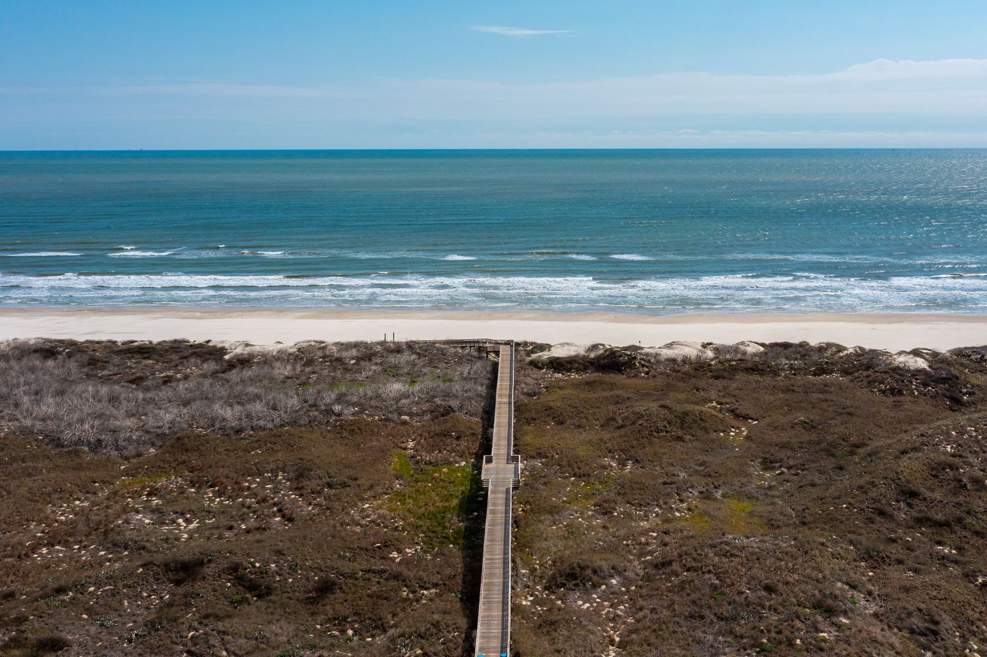 An aerial view of a beach with a wooden walkway leading to the ocean.