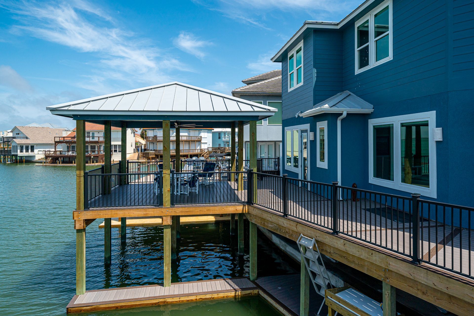 A blue house with a dock in front of it overlooking a body of water.