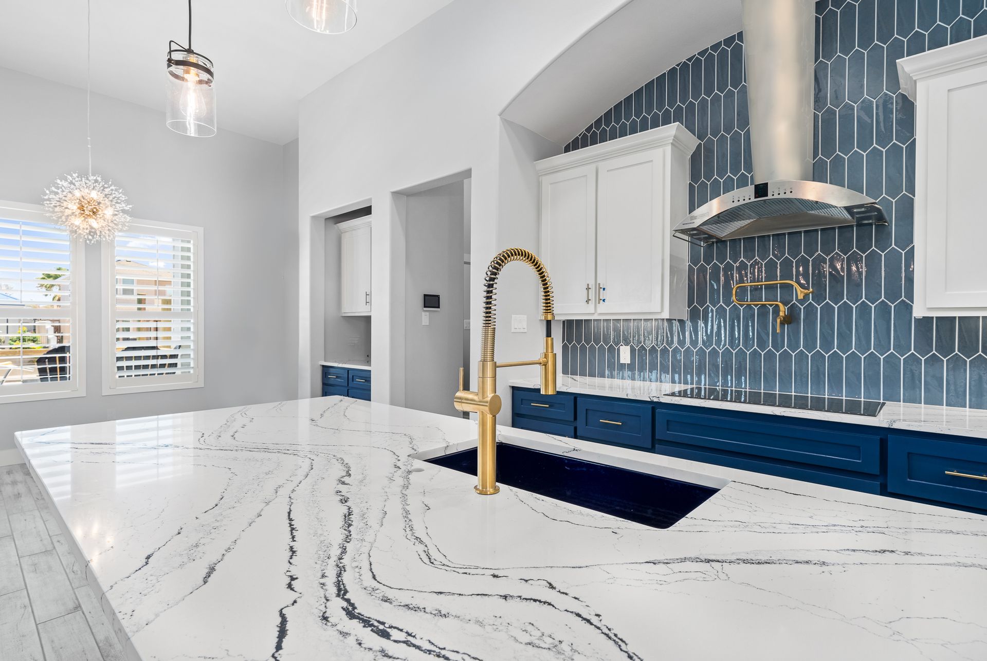A kitchen with blue cabinets , white counter tops , and a gold faucet.