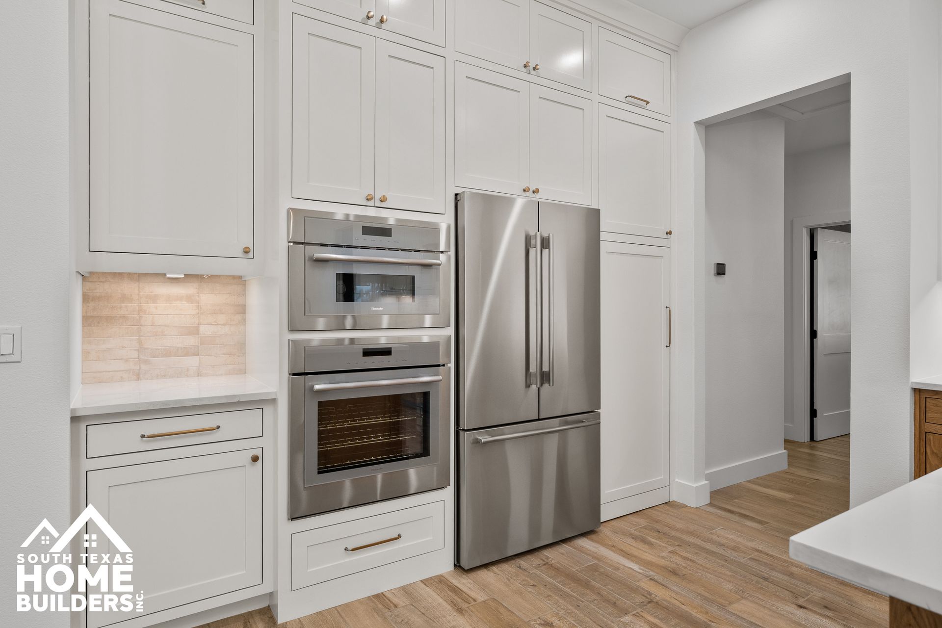 White kitchen cabinets and stainless steel appliances; a built-in oven and refrigerator.