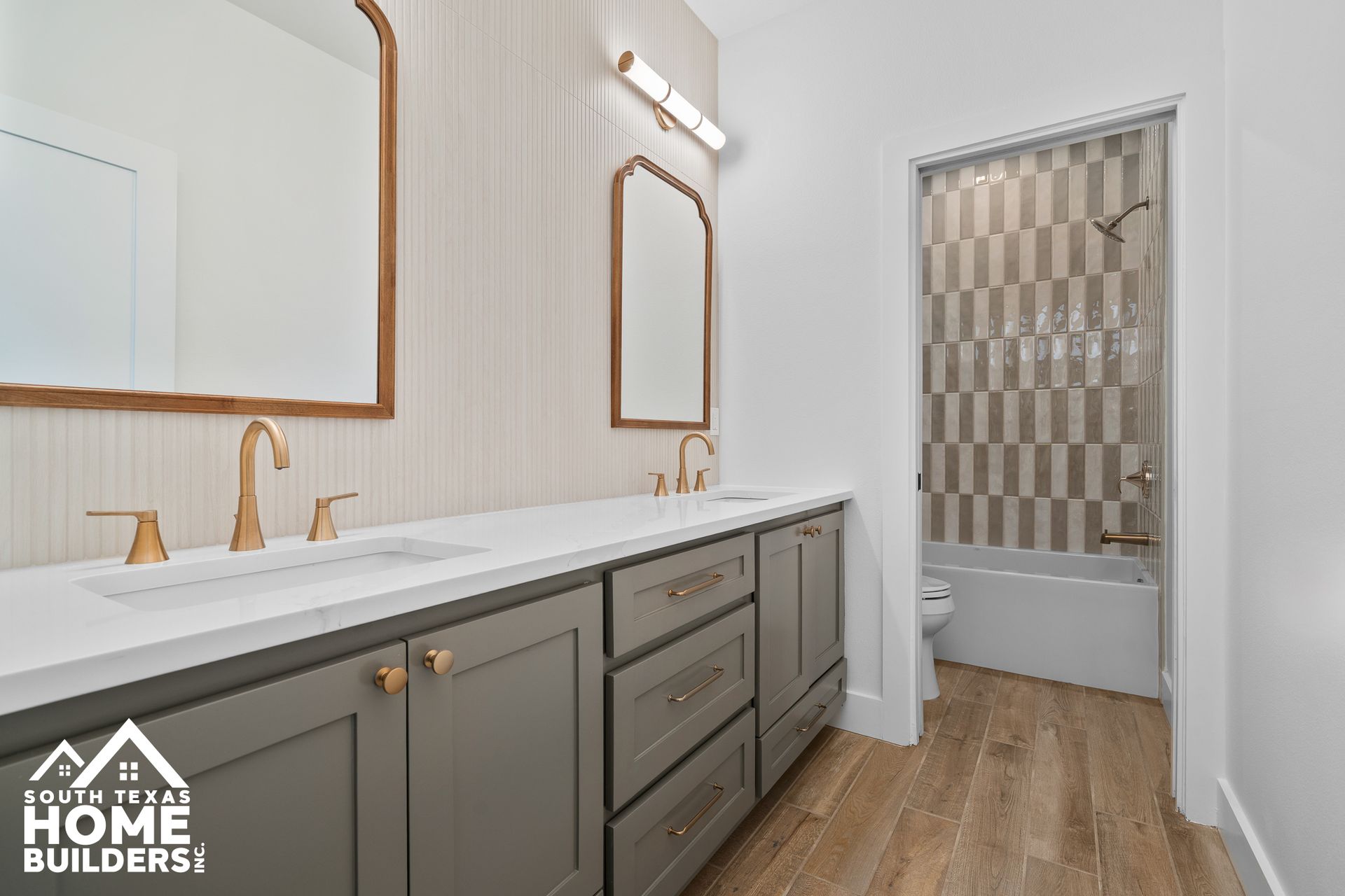 Bathroom with grey cabinets, gold fixtures, white countertop, and tiled shower.