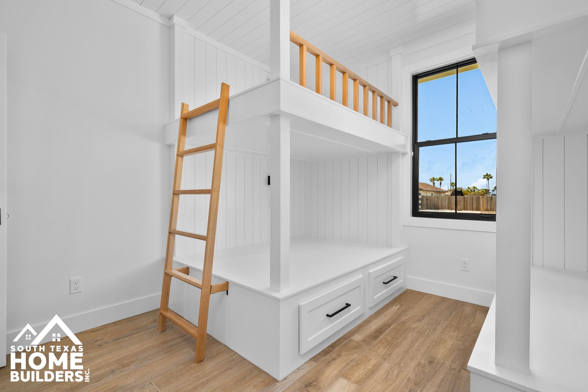 White bunk beds with wooden ladder and railing in a bright room with a window.