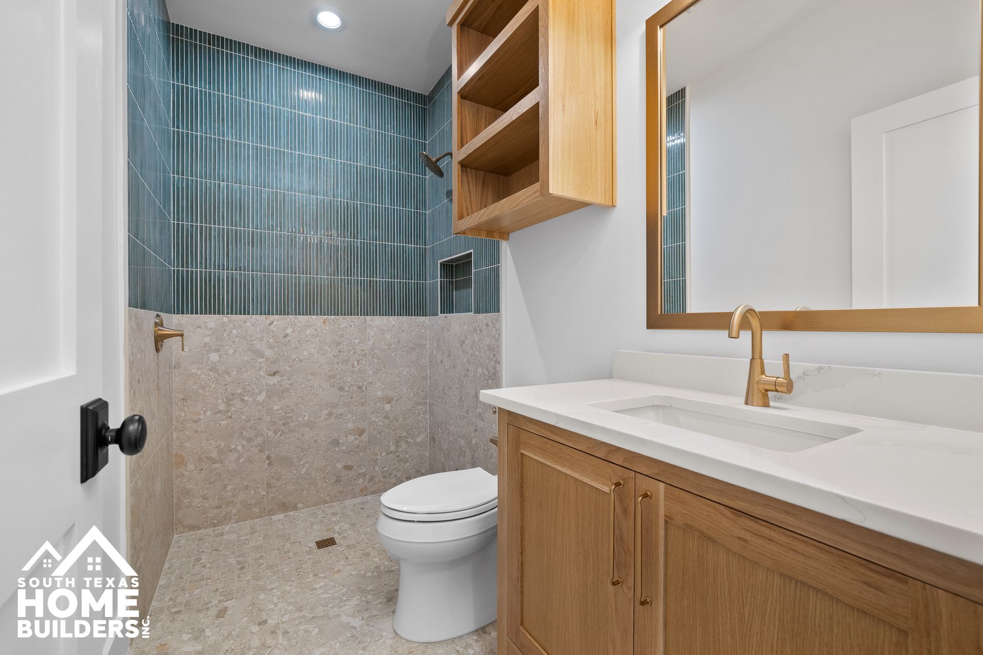 Bathroom with blue tile shower, light wood vanity, and gold fixtures.