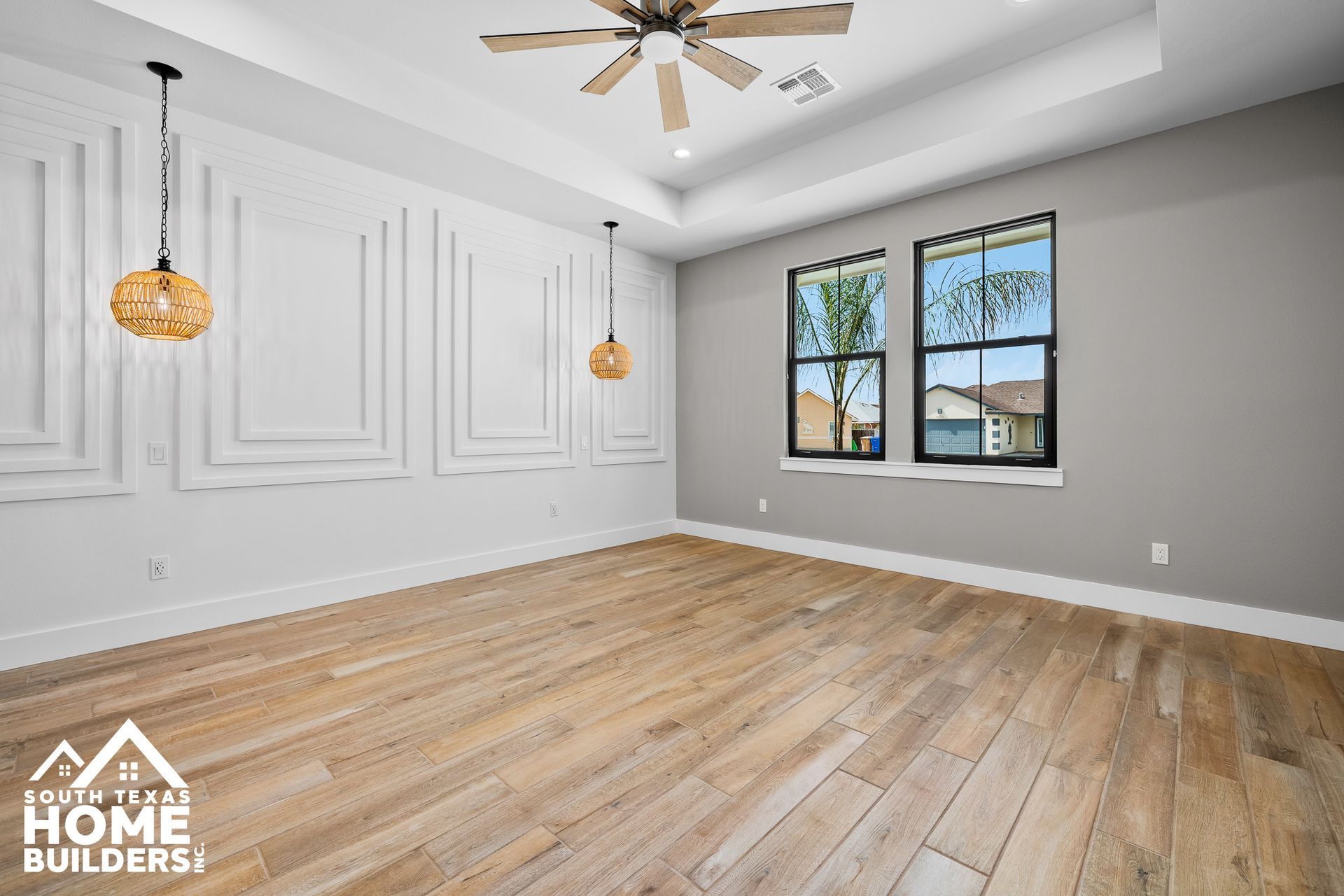 Empty bedroom with hardwood floors, decorative wall molding, two windows, and hanging pendant lights.