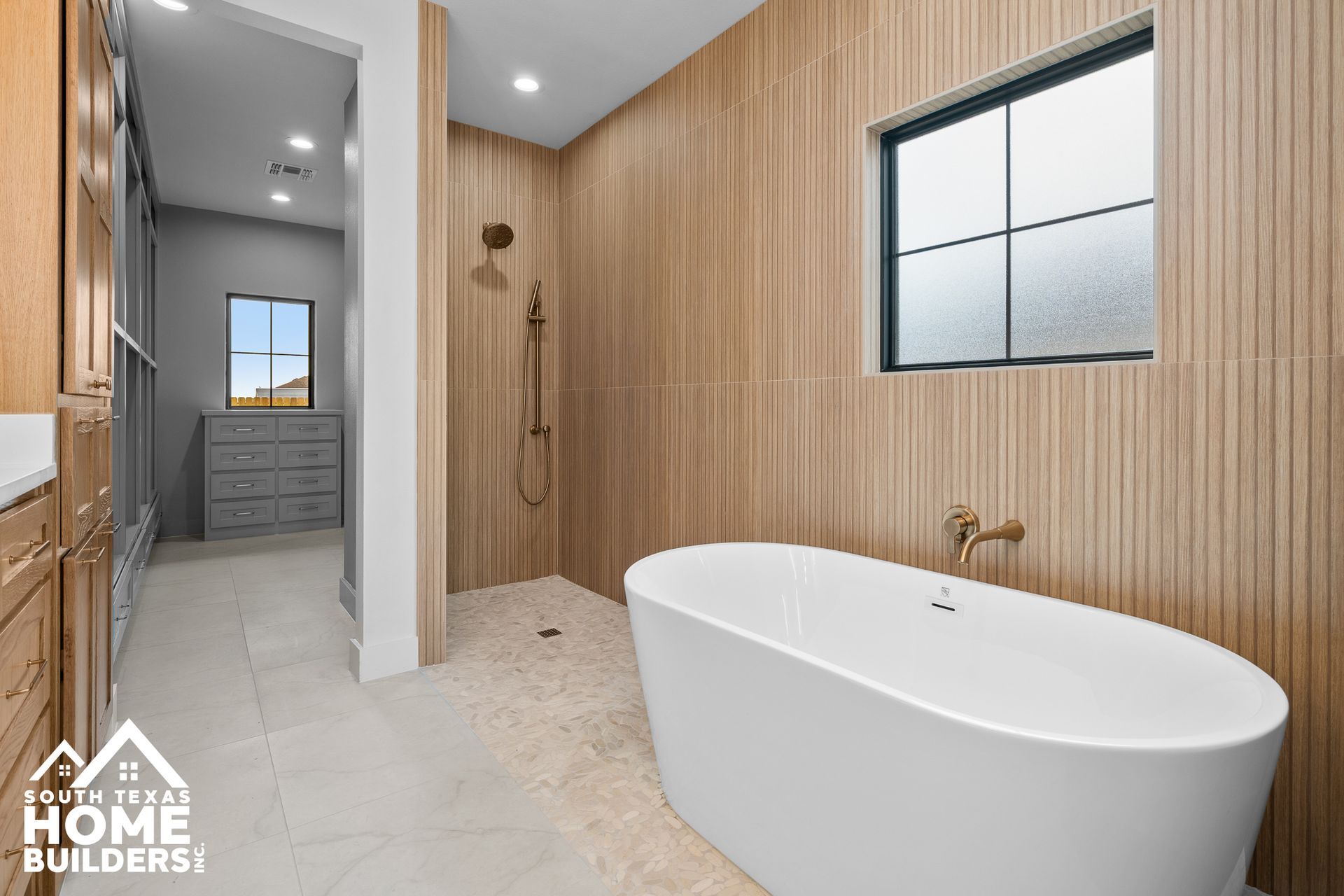 Modern bathroom with wooden accent wall, freestanding tub, walk-in shower, and closet entrance.