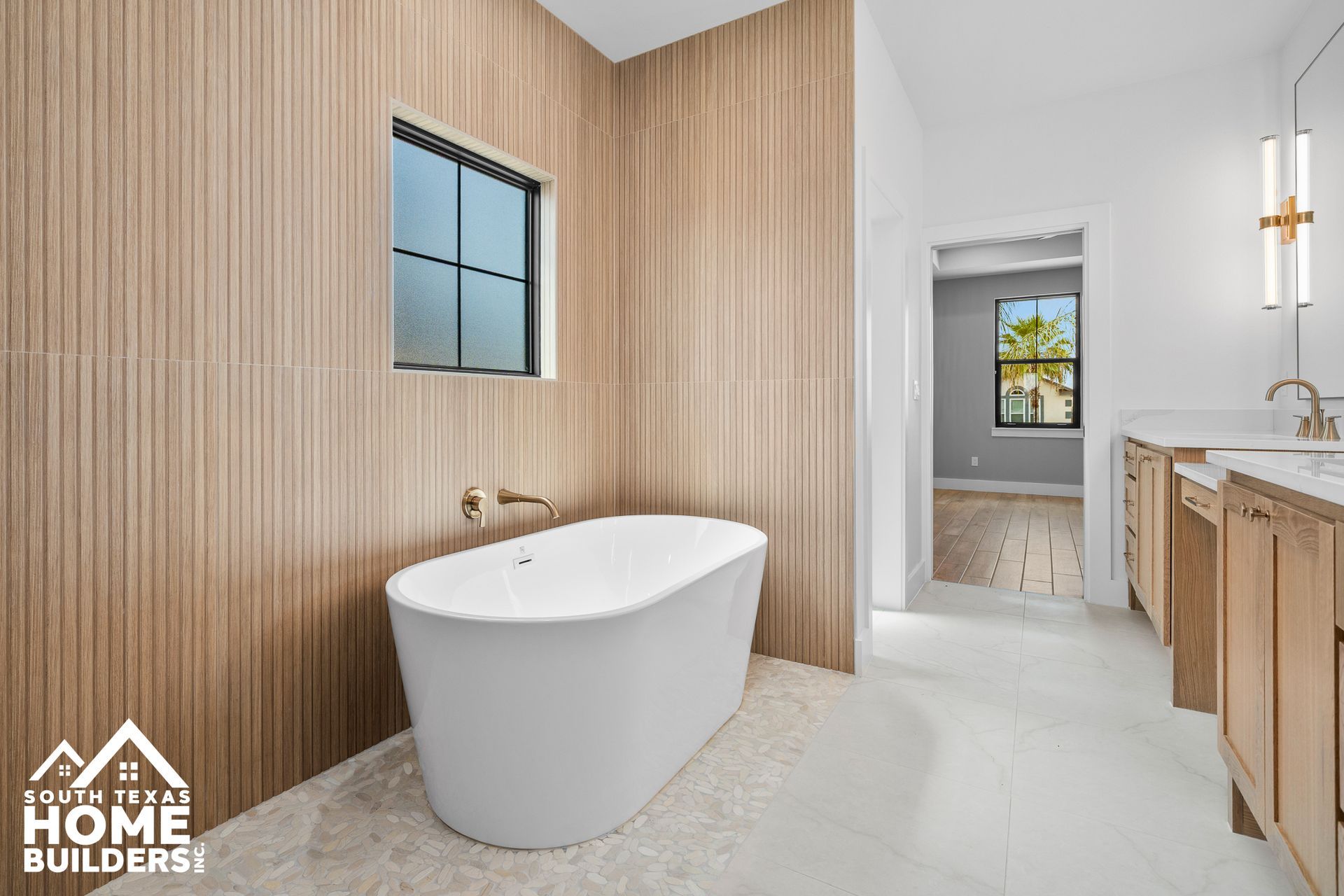 Bathroom with a white tub, light wood-toned wall, and a window. Light-colored tile floor.
