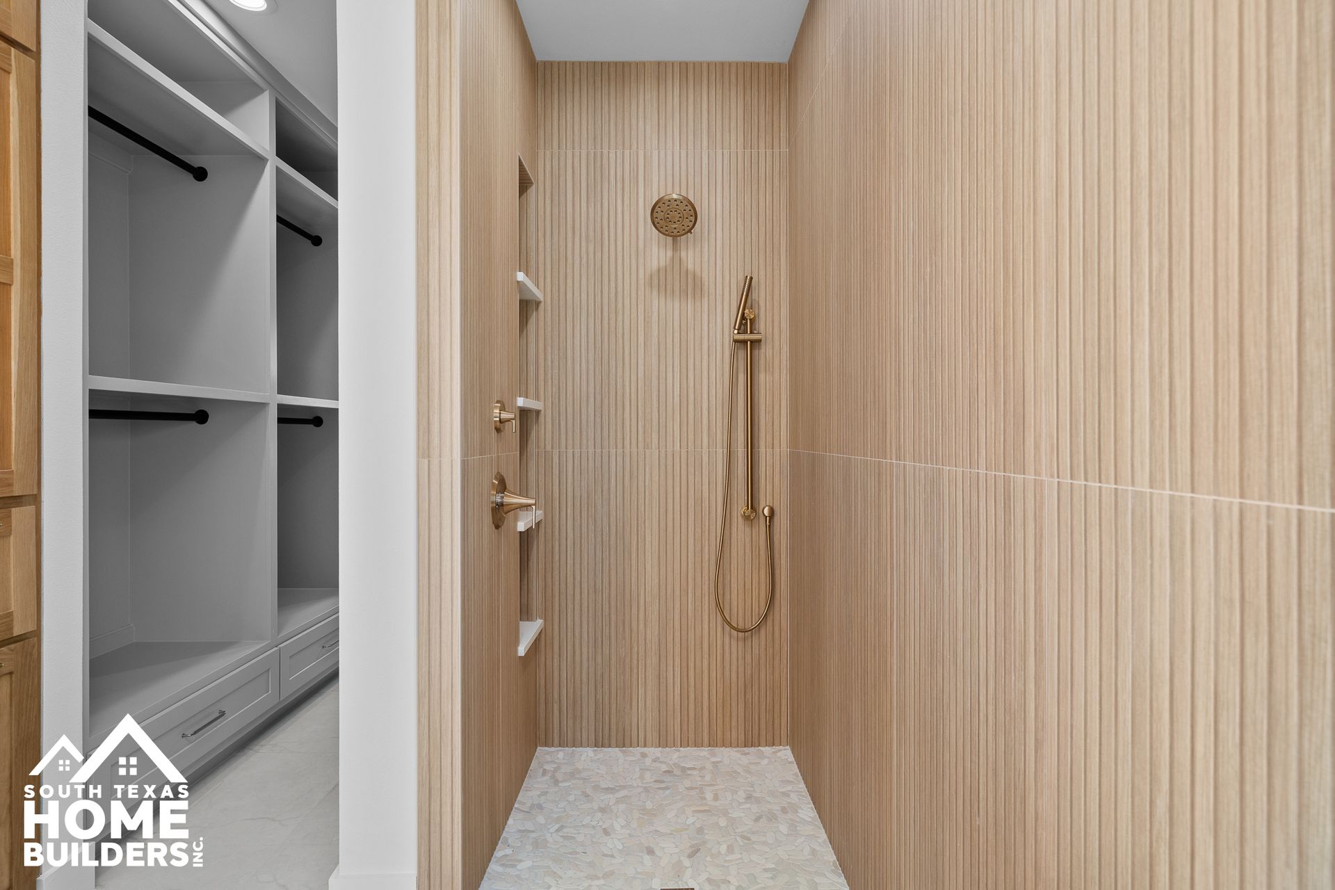 Walk-in shower with vertical wood-paneled walls, gold fixtures, and terrazzo floor. Closets visible on the left.