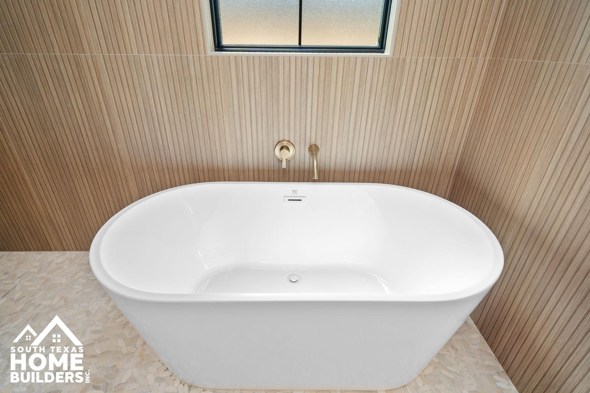 White oval bathtub in a modern bathroom with wood-look tile walls and a small window above.