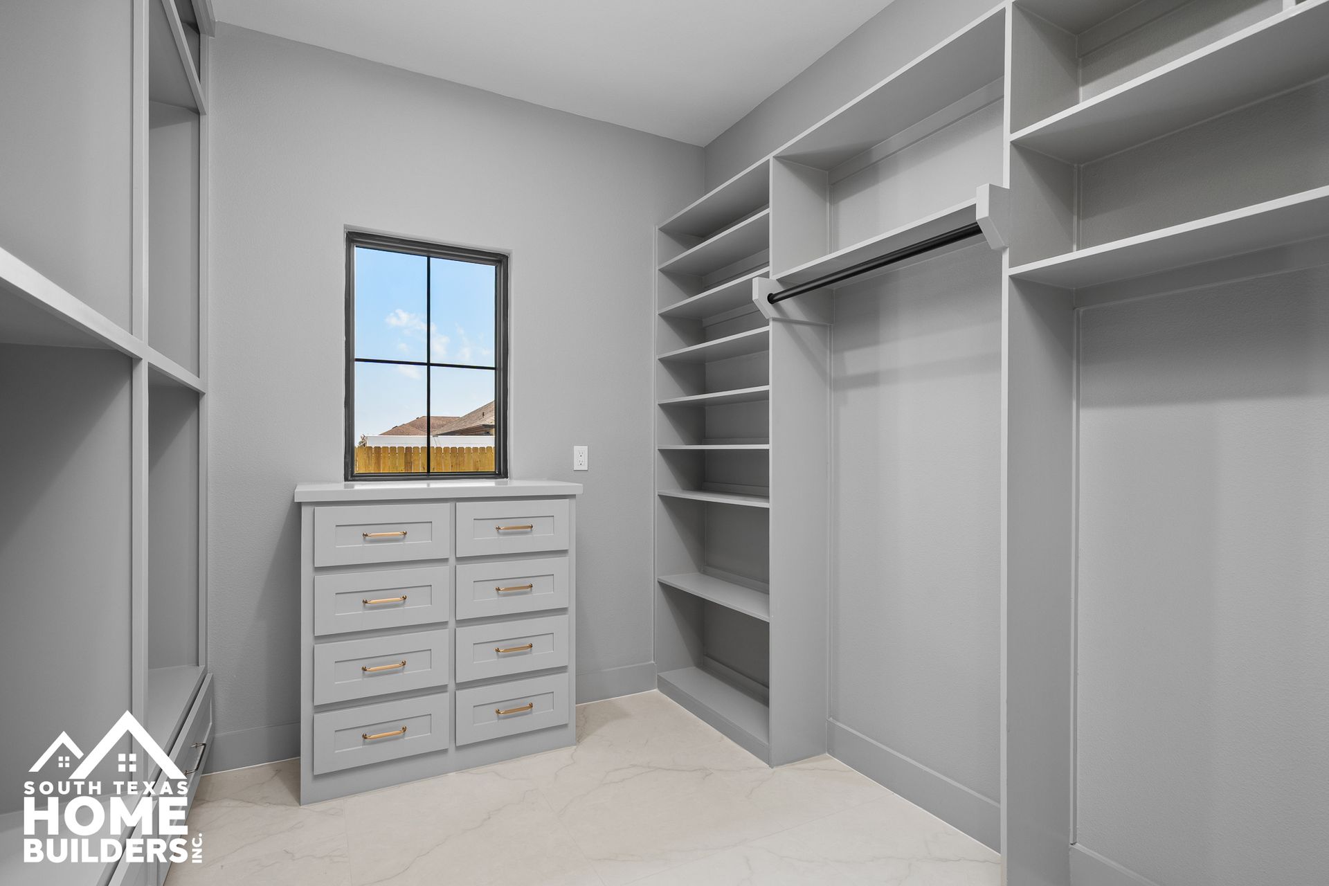 Gray walk-in closet with built-in shelves and drawers. A small window with a view is centered.