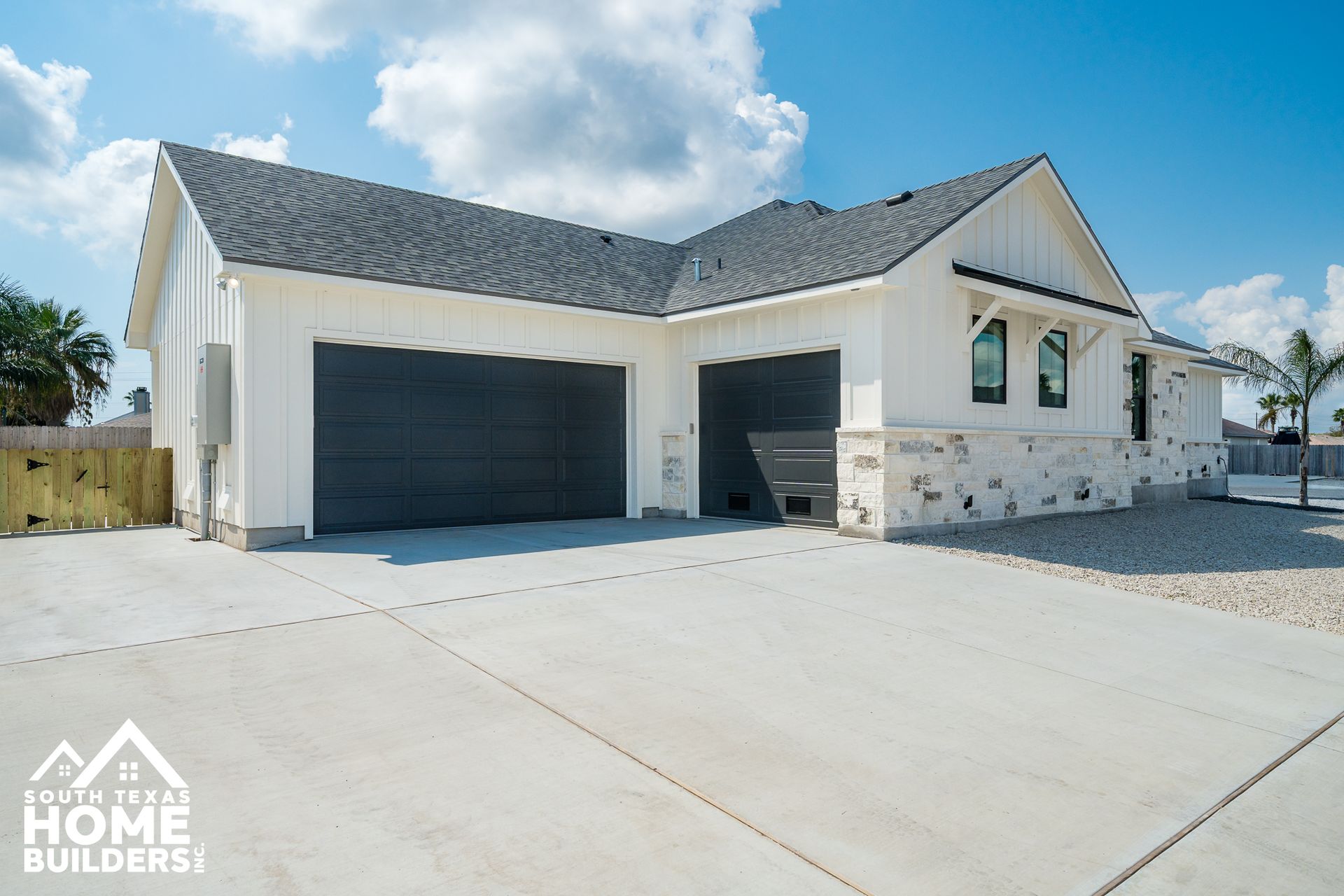 White farmhouse-style house with gray garage doors, blue sky, and concrete driveway.