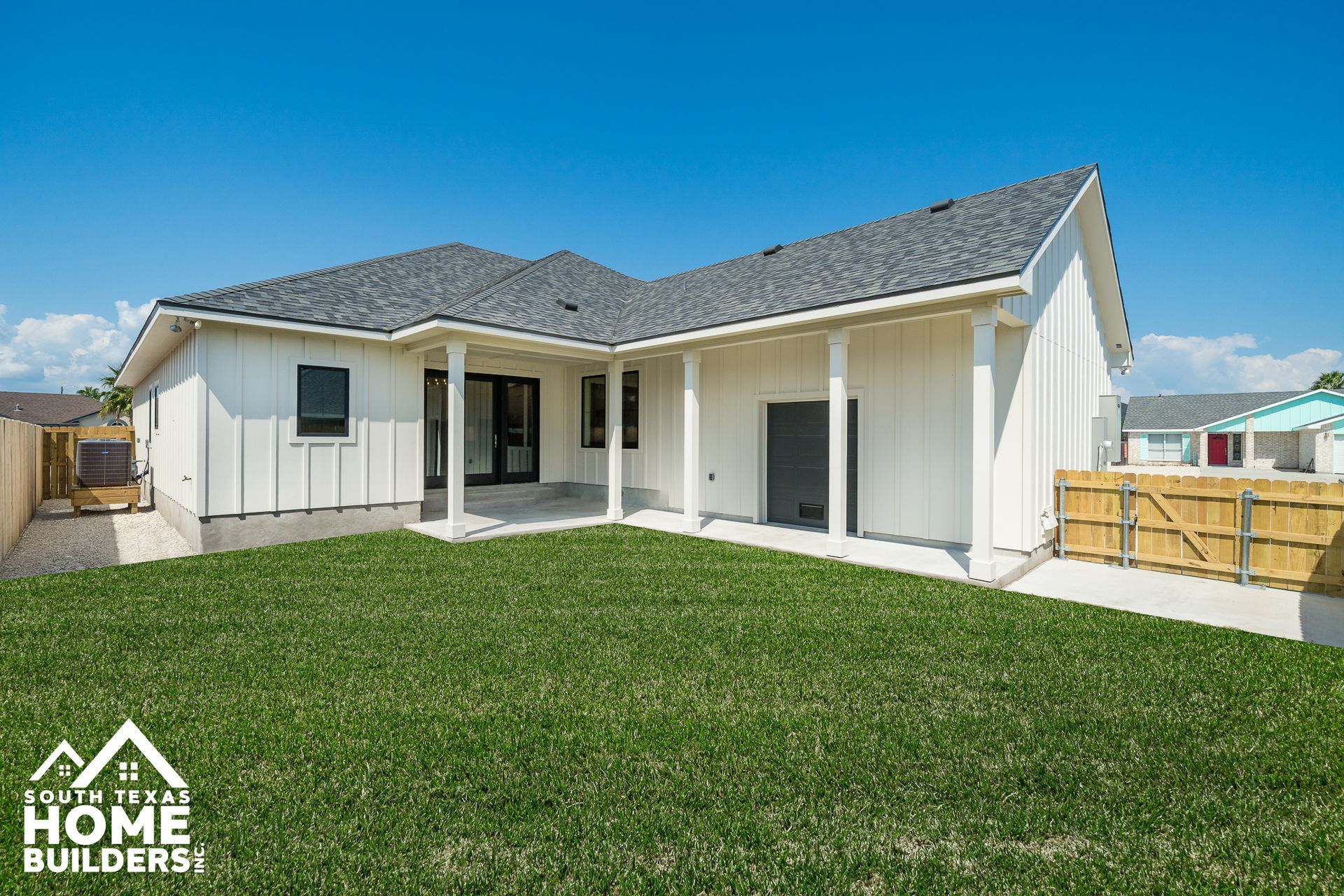 White house with dark gray roof, backyard lawn, blue sky.