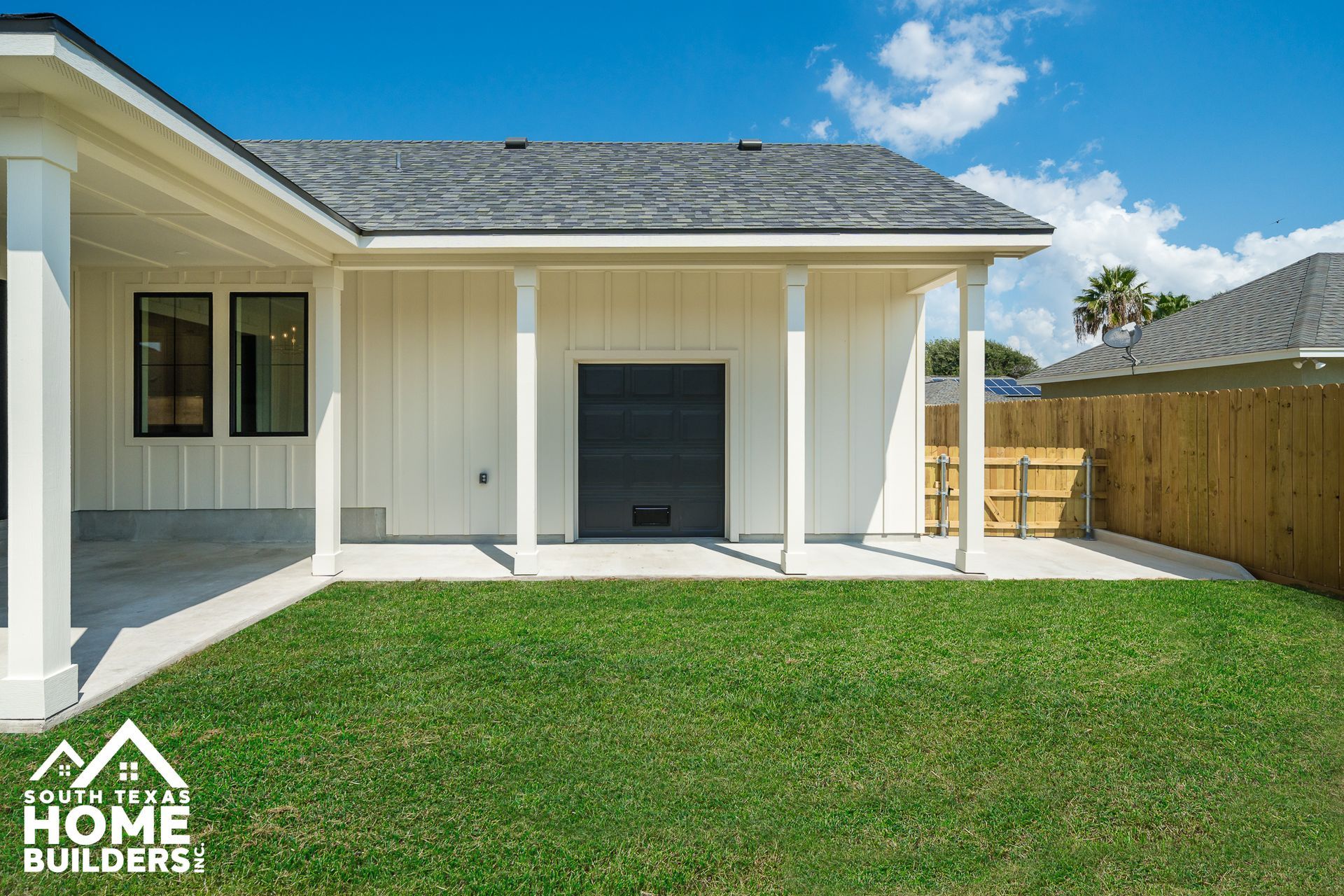 White house exterior with porch, black garage door, and green lawn on a sunny day.