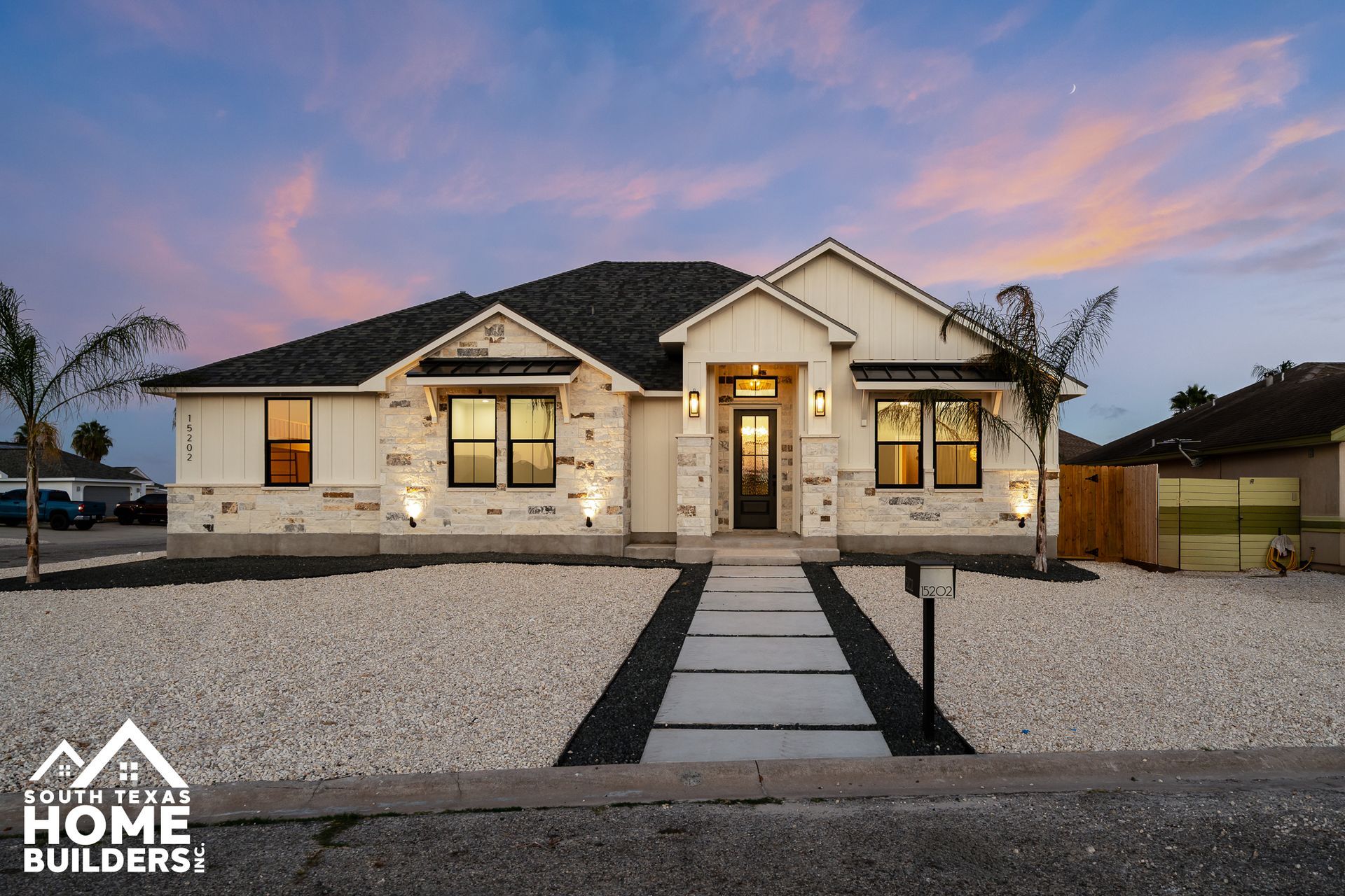 Modern, white house with stone accents and a gray roof at dusk.