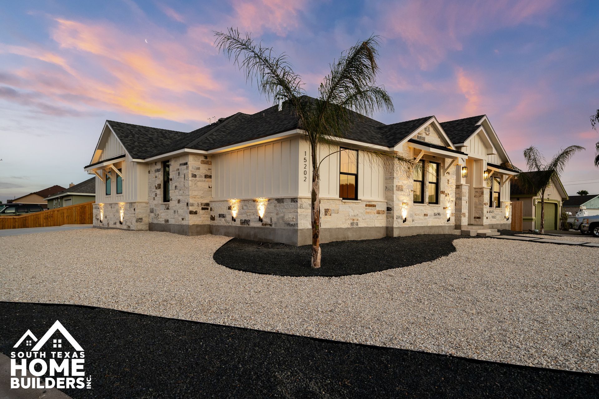 Modern home with stone and white siding exterior, under a colorful sunset sky.