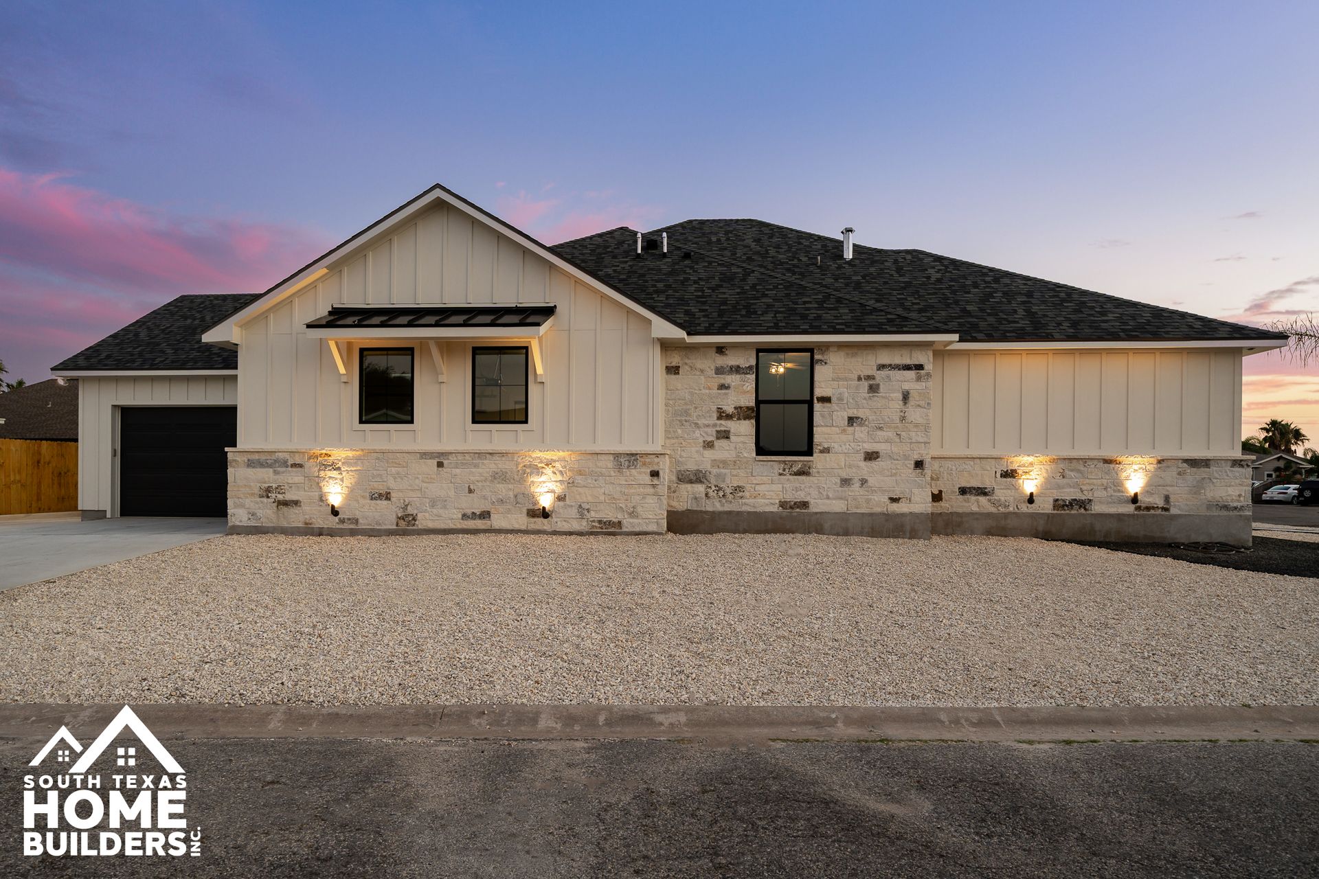 Modern home exterior with white siding, stone accents, and gravel yard at dusk.