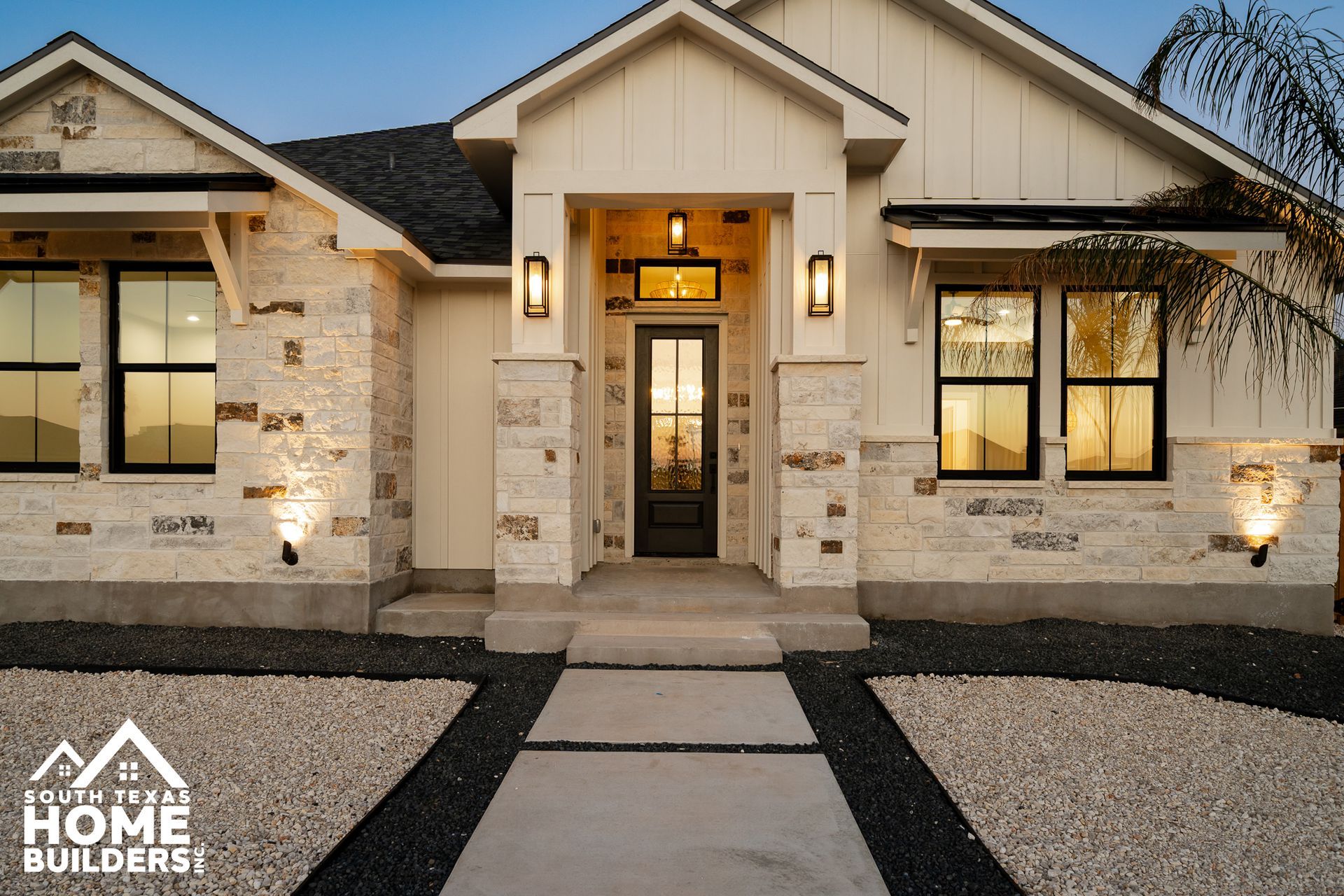 Exterior of a modern house with stone facade, black-framed windows, and a paved walkway.