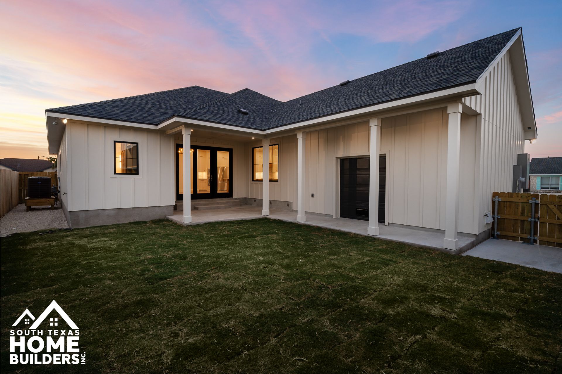 Rear view of a white modern house with a green lawn. Includes a porch, and a colorful sunset.