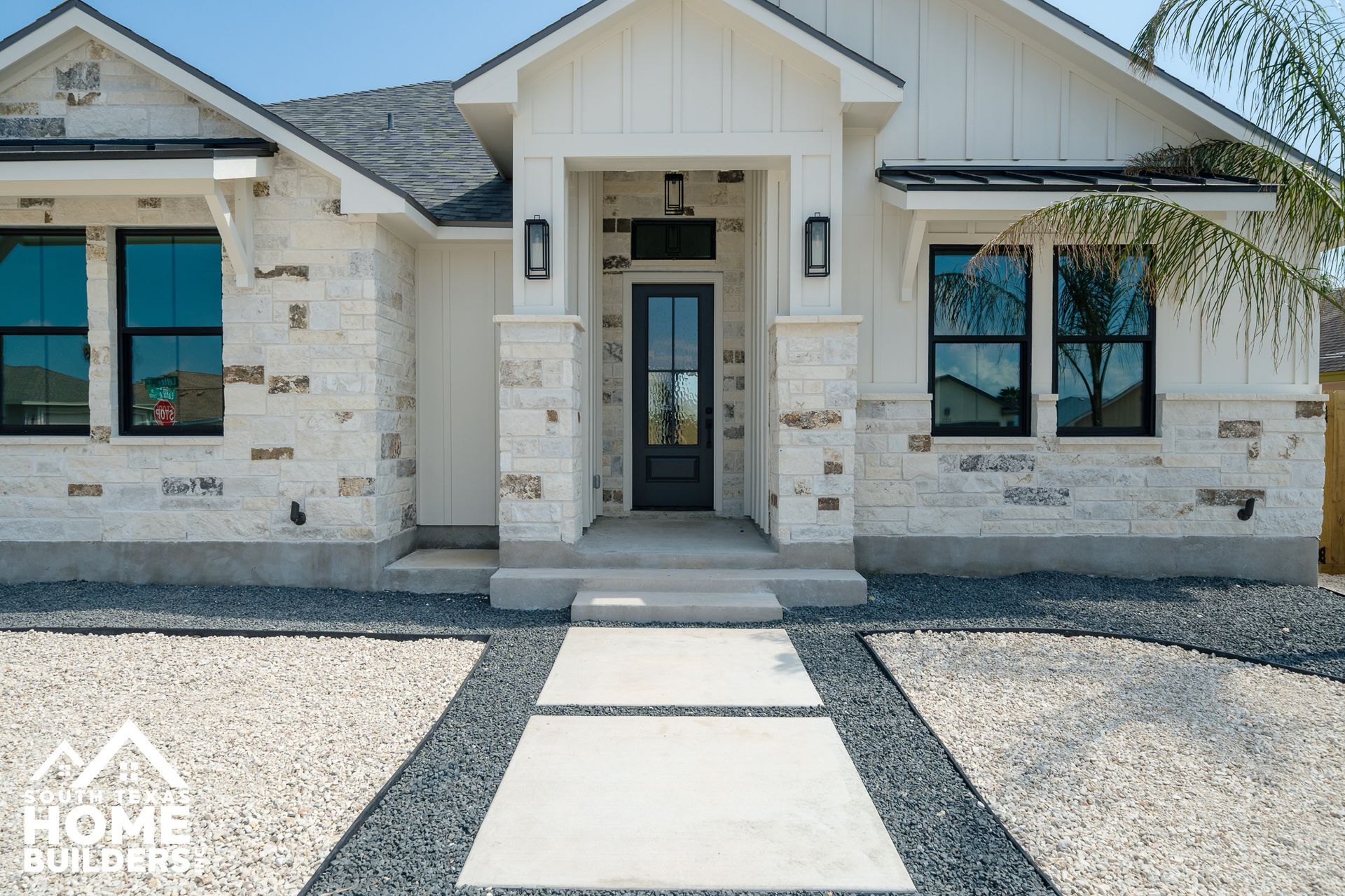 Exterior of a modern house with stone facade, dark-framed windows, and a paved walkway.