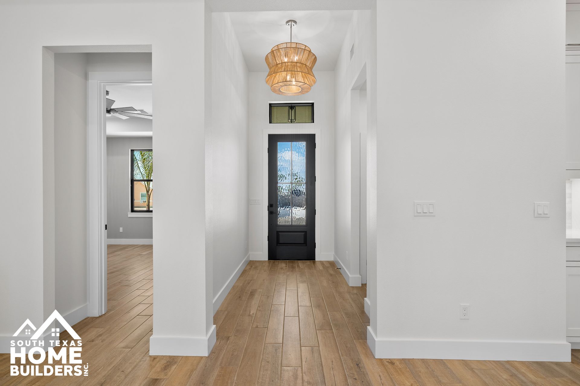 Hallway with wood floors, white walls, black front door, and a chandelier.