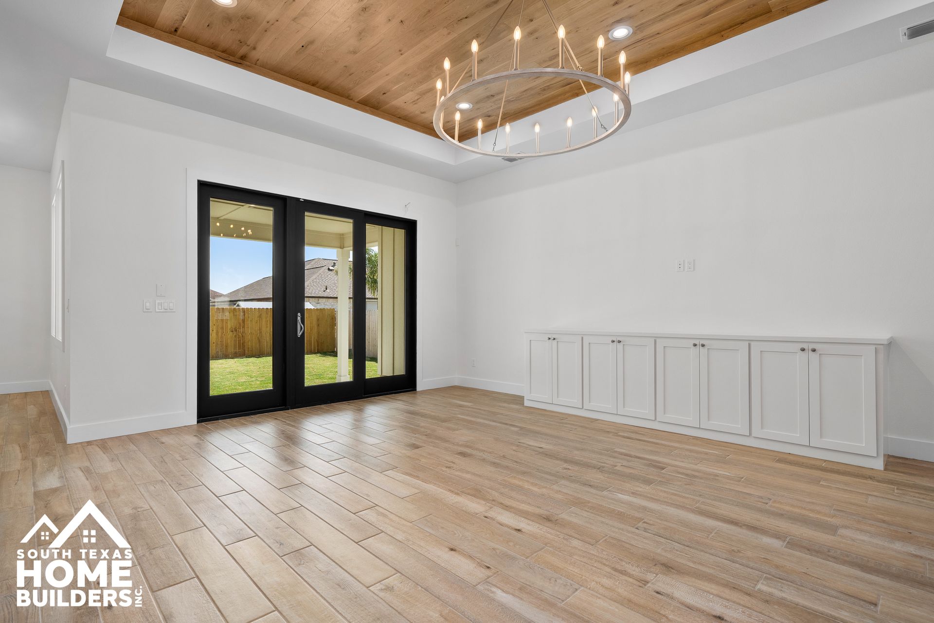 Empty dining room with wood ceiling, glass doors to the backyard, white cabinets, light wood floor, and chandelier.