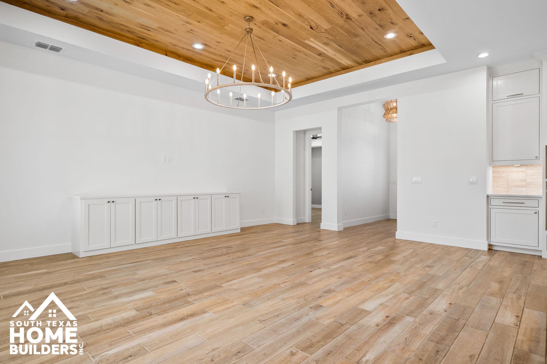 Empty room with wood ceiling, wood floor, white walls and cabinets, chandelier.