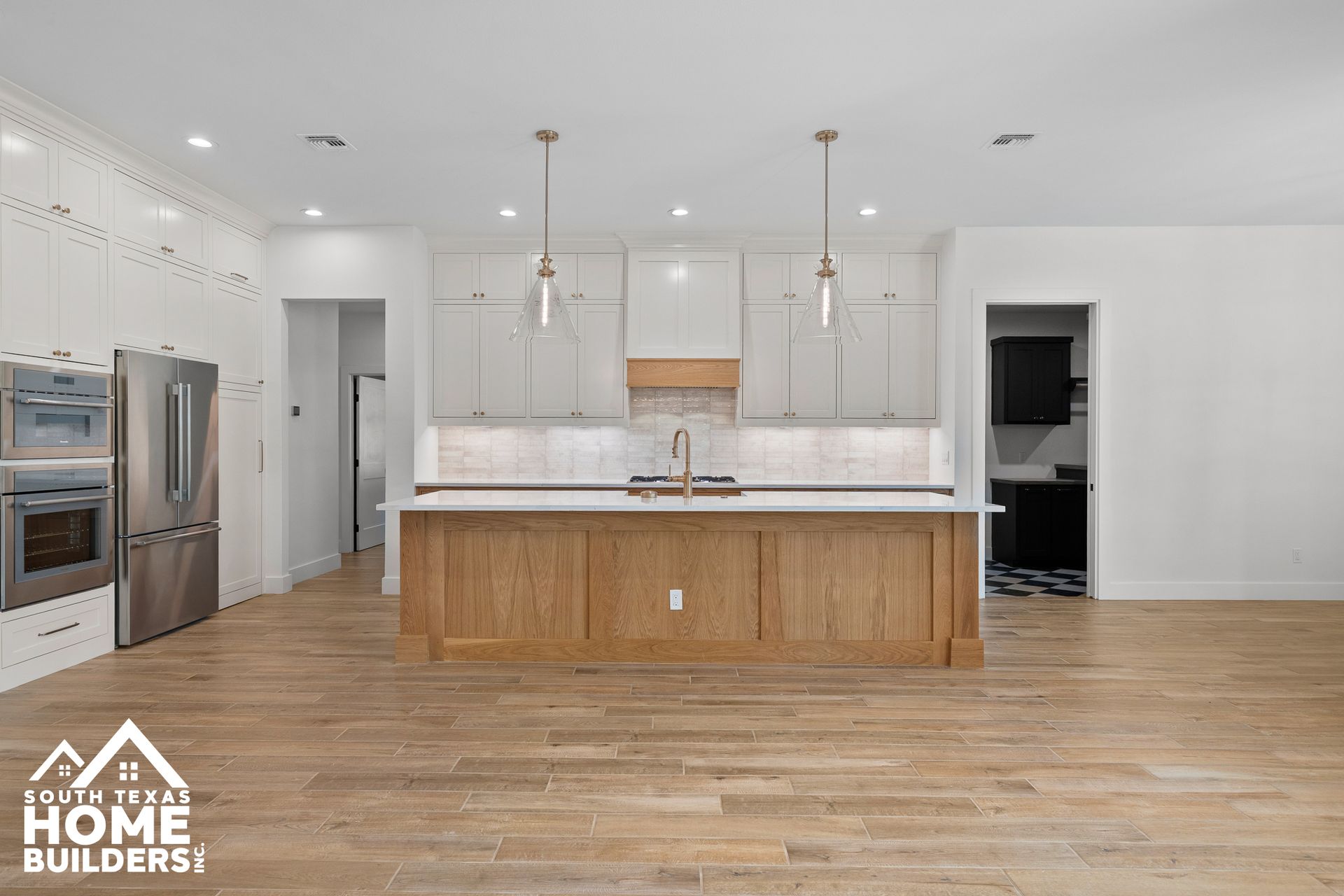 Modern kitchen with wood island and white cabinets, light wood flooring and stainless steel appliances.