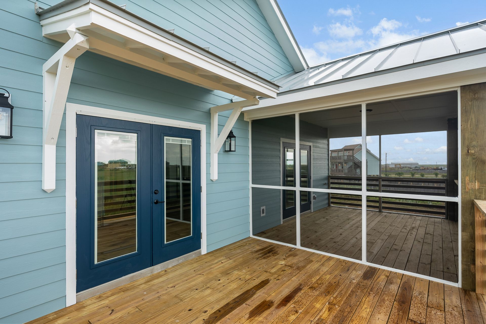 Blue house exterior with double doors, screened porch, and wooden deck.