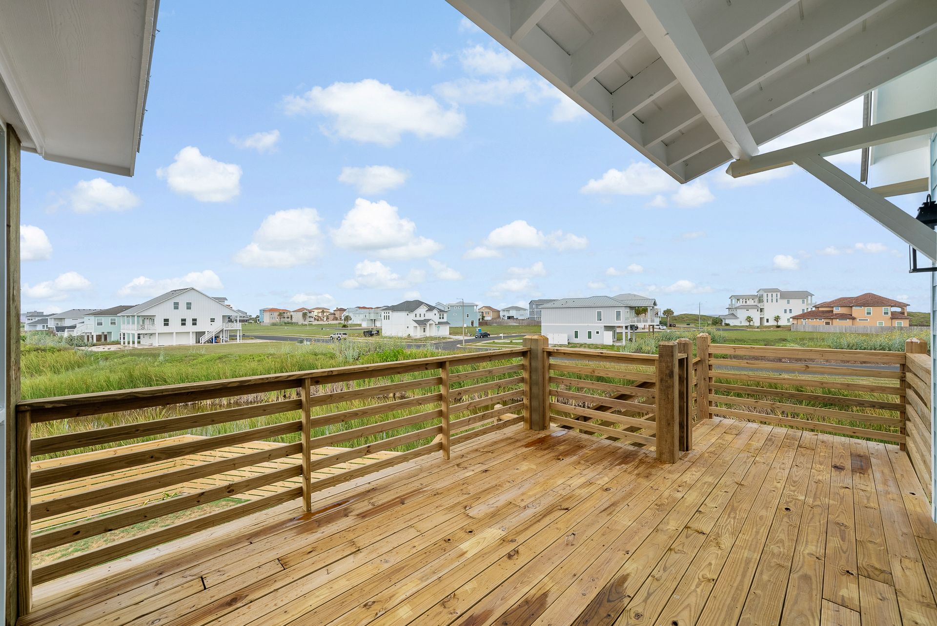 Wooden deck with railing overlooking a grassy area and houses under a cloudy sky.