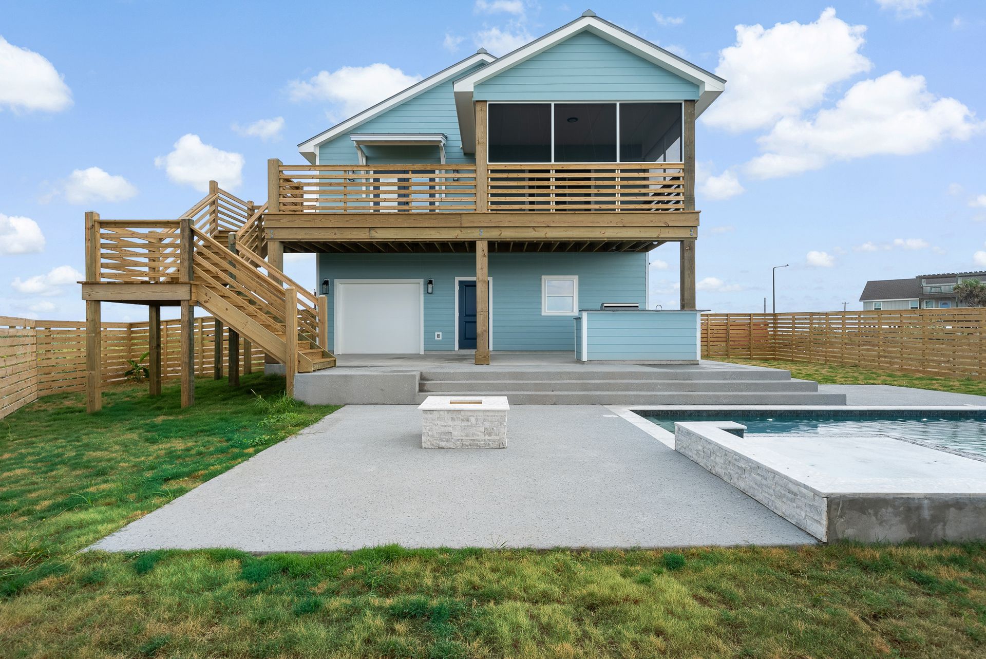 Beach house with blue siding, raised deck, and pool on a sunny day.