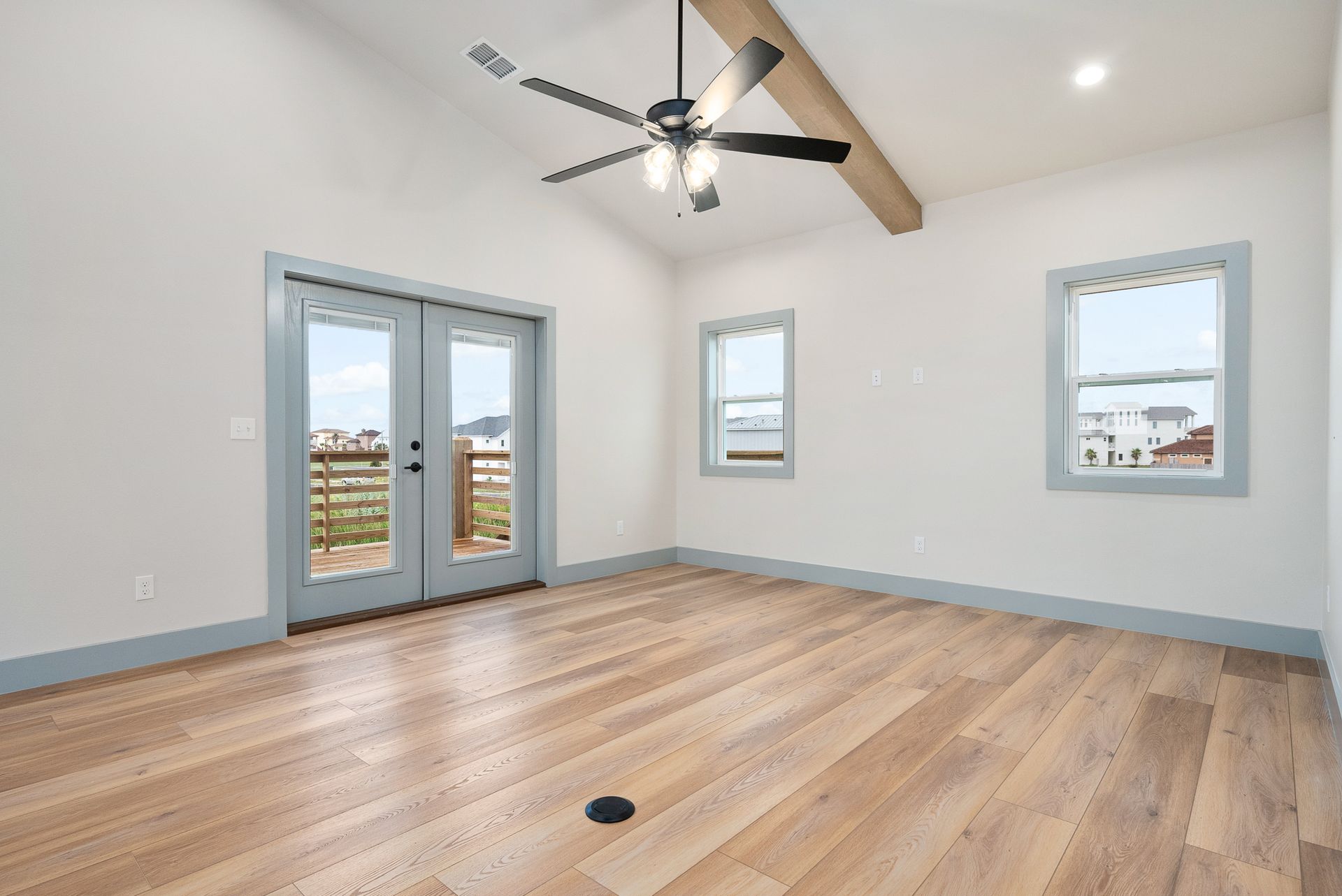 Empty room with wood floors, blue trim, vaulted ceiling, and patio doors.
