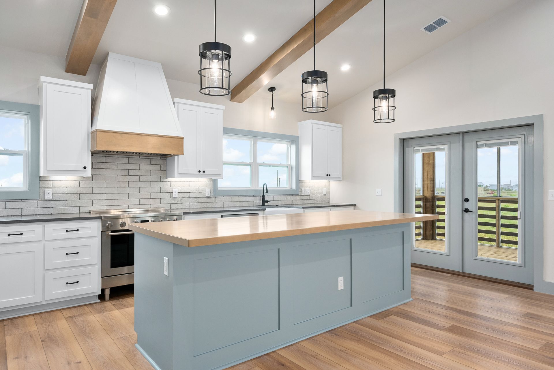 Modern kitchen with white cabinets, blue island, wood accents, and pendant lights.