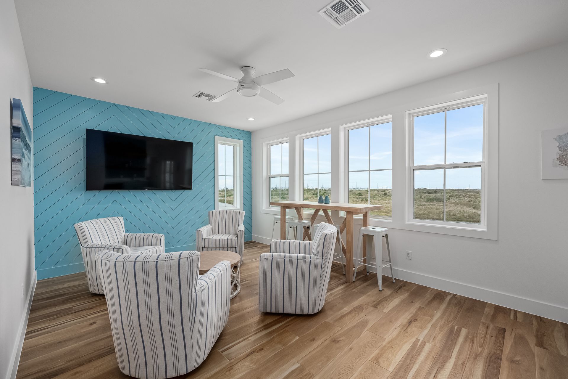 A living room with a blue wall , chairs , a table and a flat screen tv.