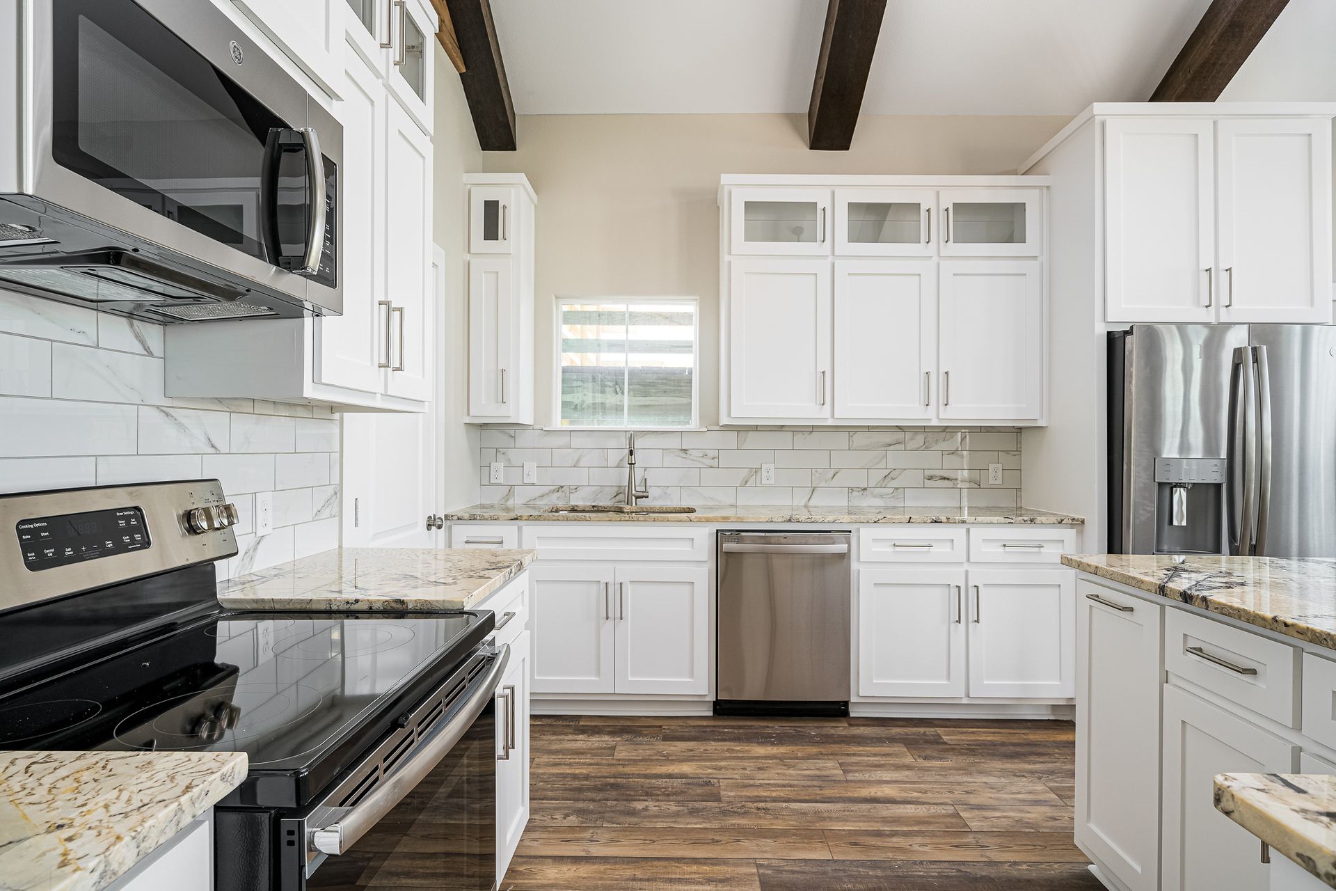 A kitchen with white cabinets , stainless steel appliances , granite counter tops and wooden floors.
