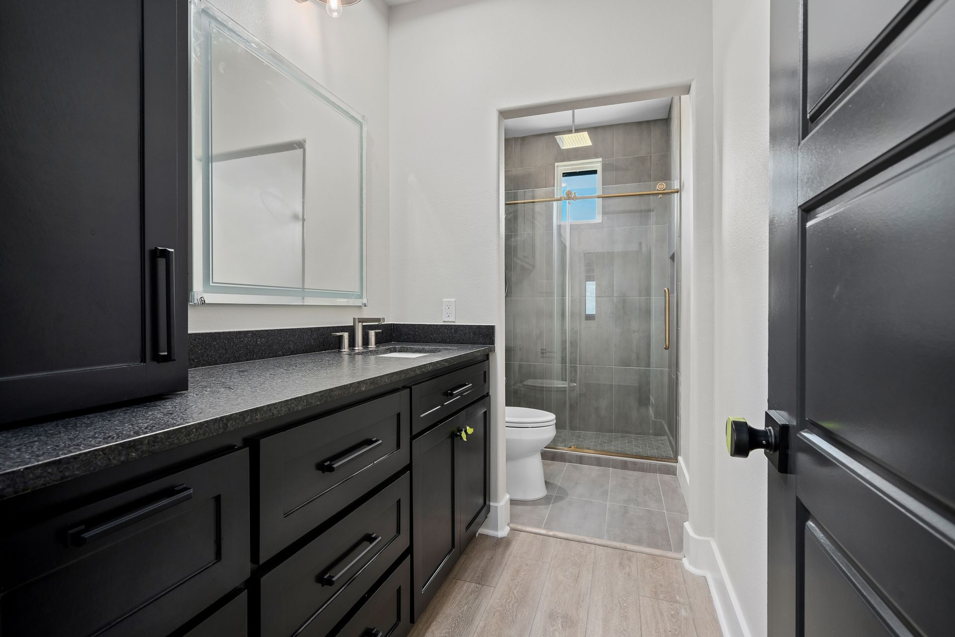 A bathroom with black cabinets , a toilet , and a walk in shower.