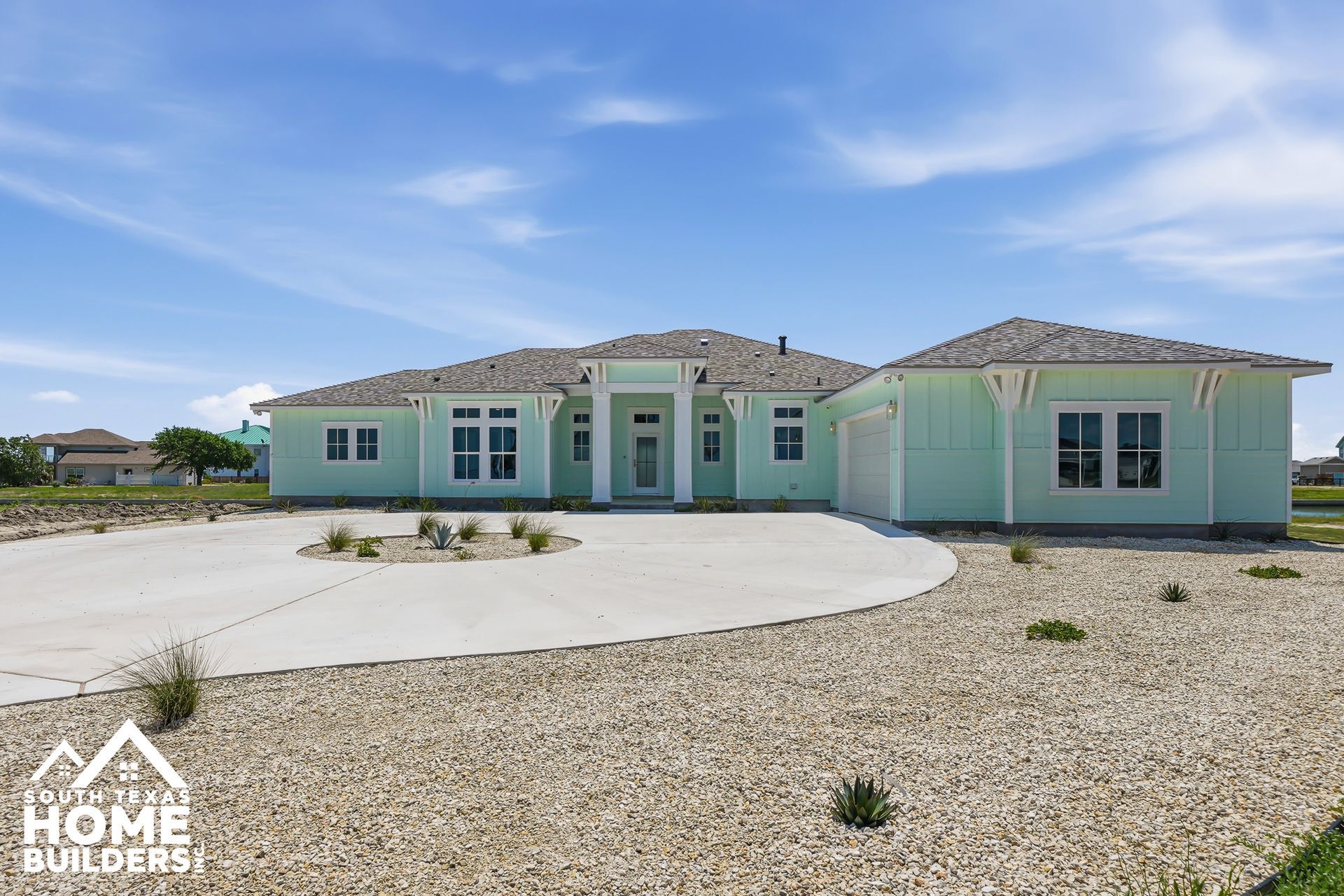 New light green single-story house with a curved white driveway and gravel lot under a blue sky
