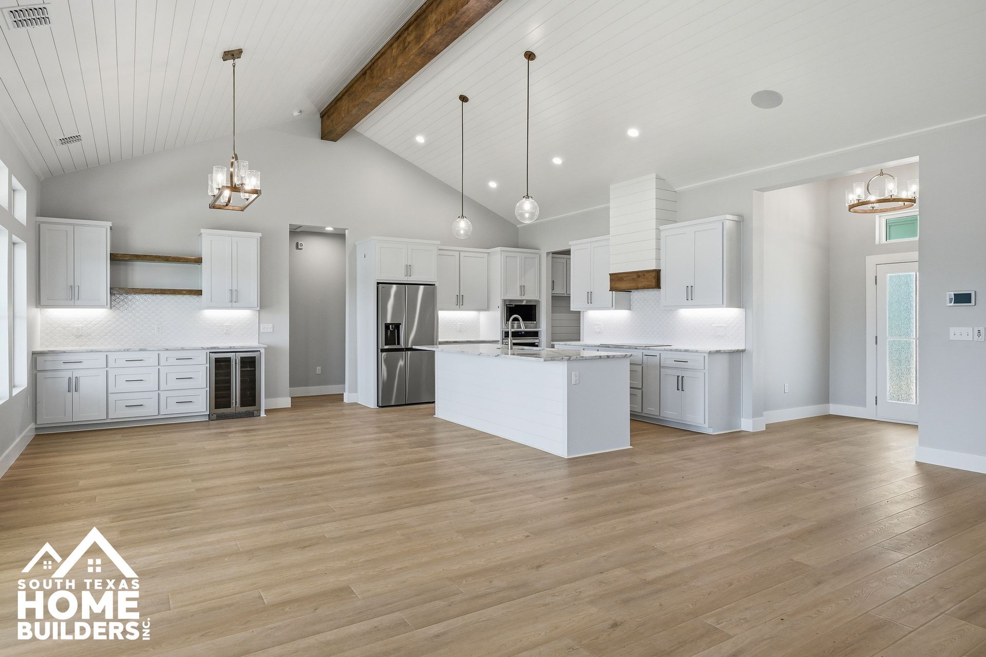 Bright modern kitchen and living area with white cabinets, island, stainless appliances, and wood floors